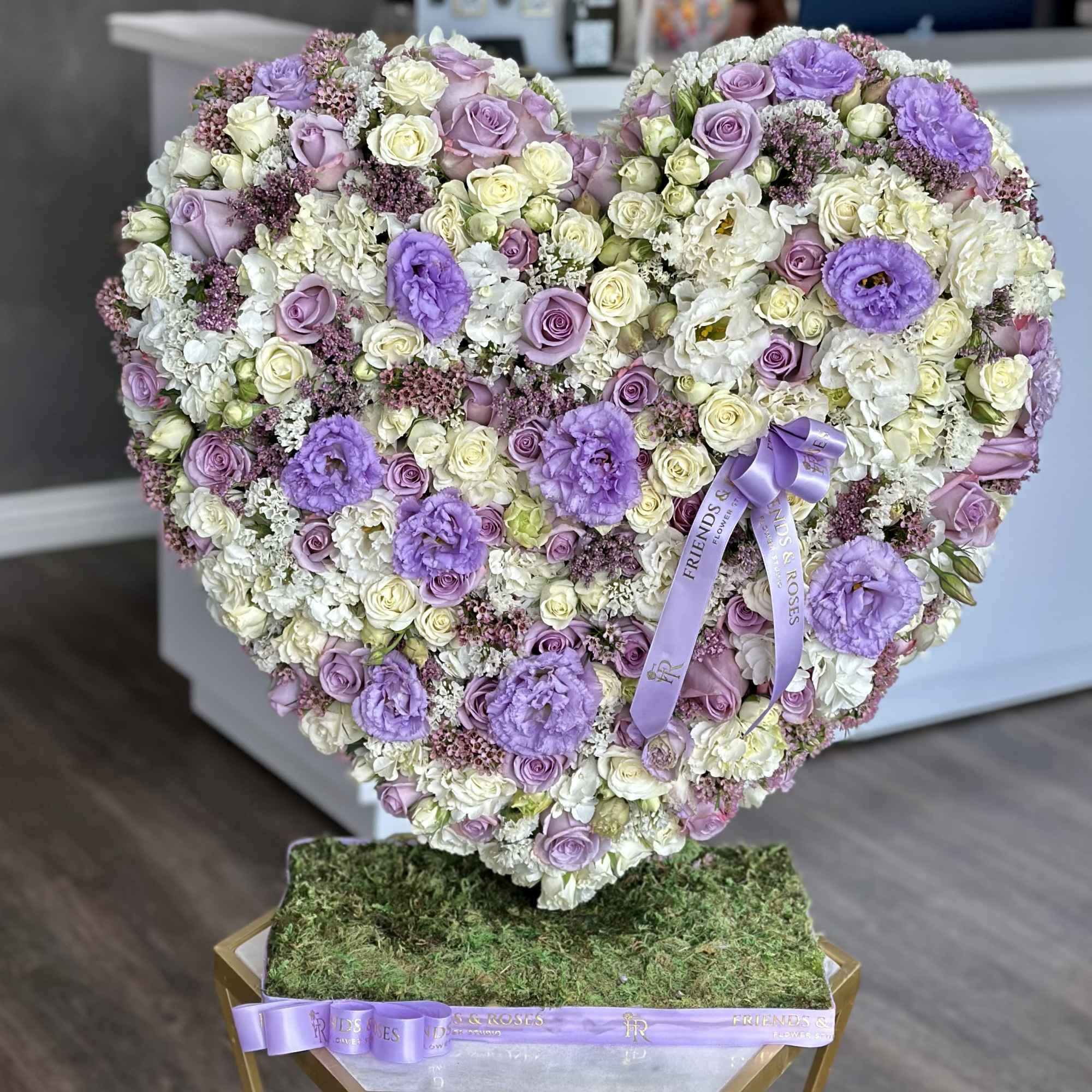 Heart-shaped floral arrangement of lavender, white, and cream roses with a purple ribbon