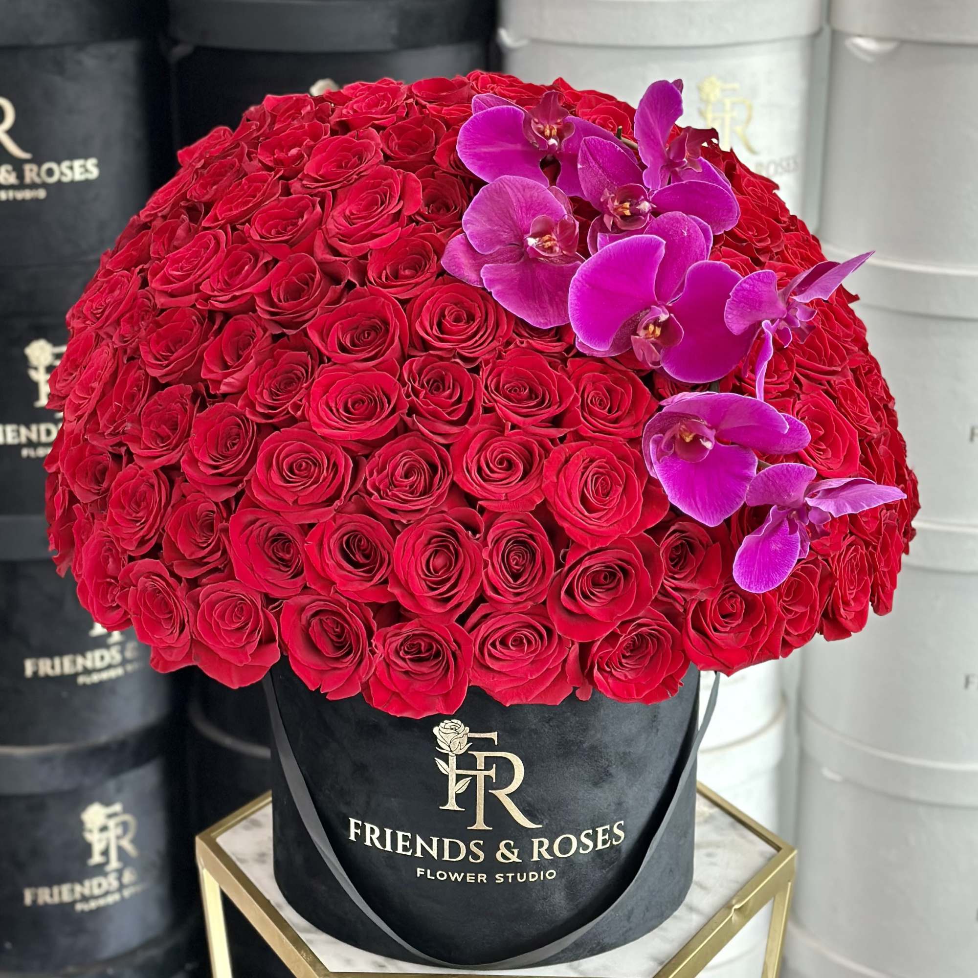 Large red rose arrangement with magenta orchids in a black hat box