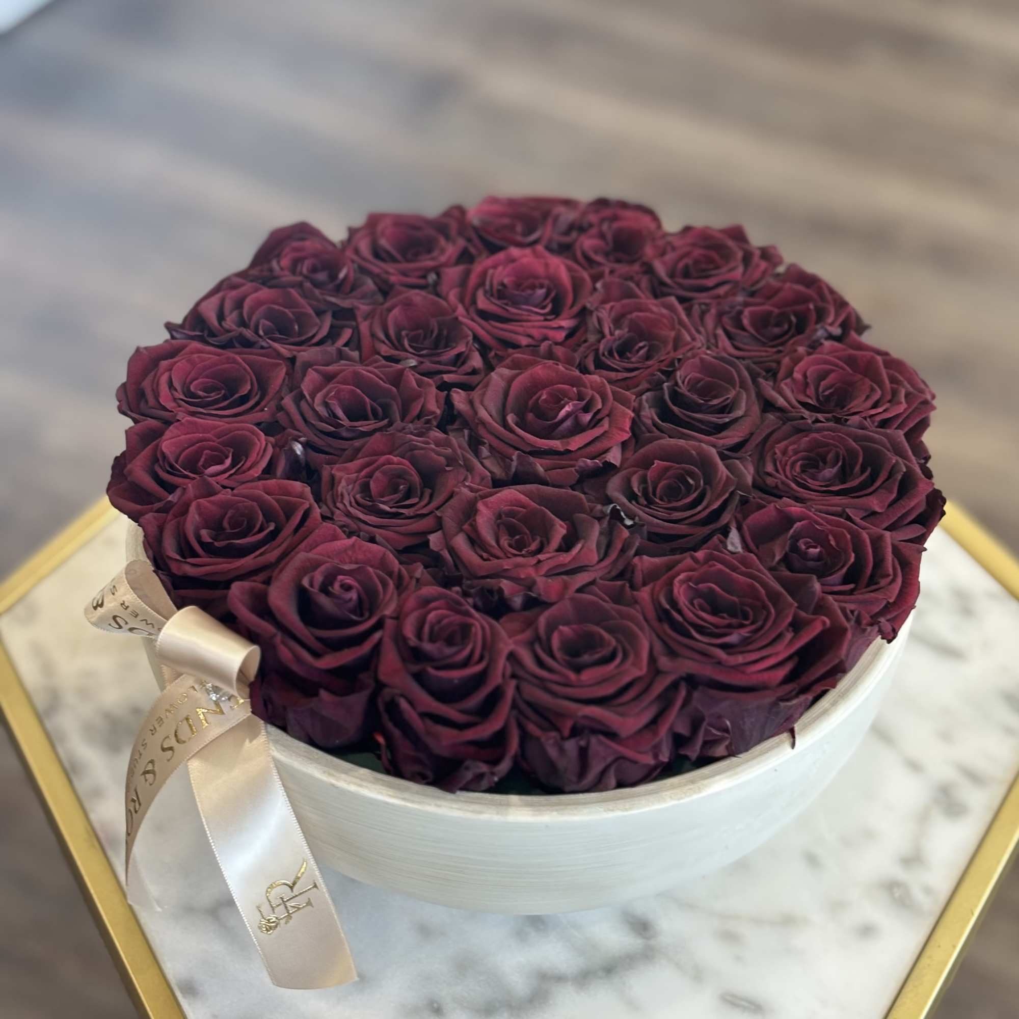 Round box filled with deep burgundy roses and a satin ribbon