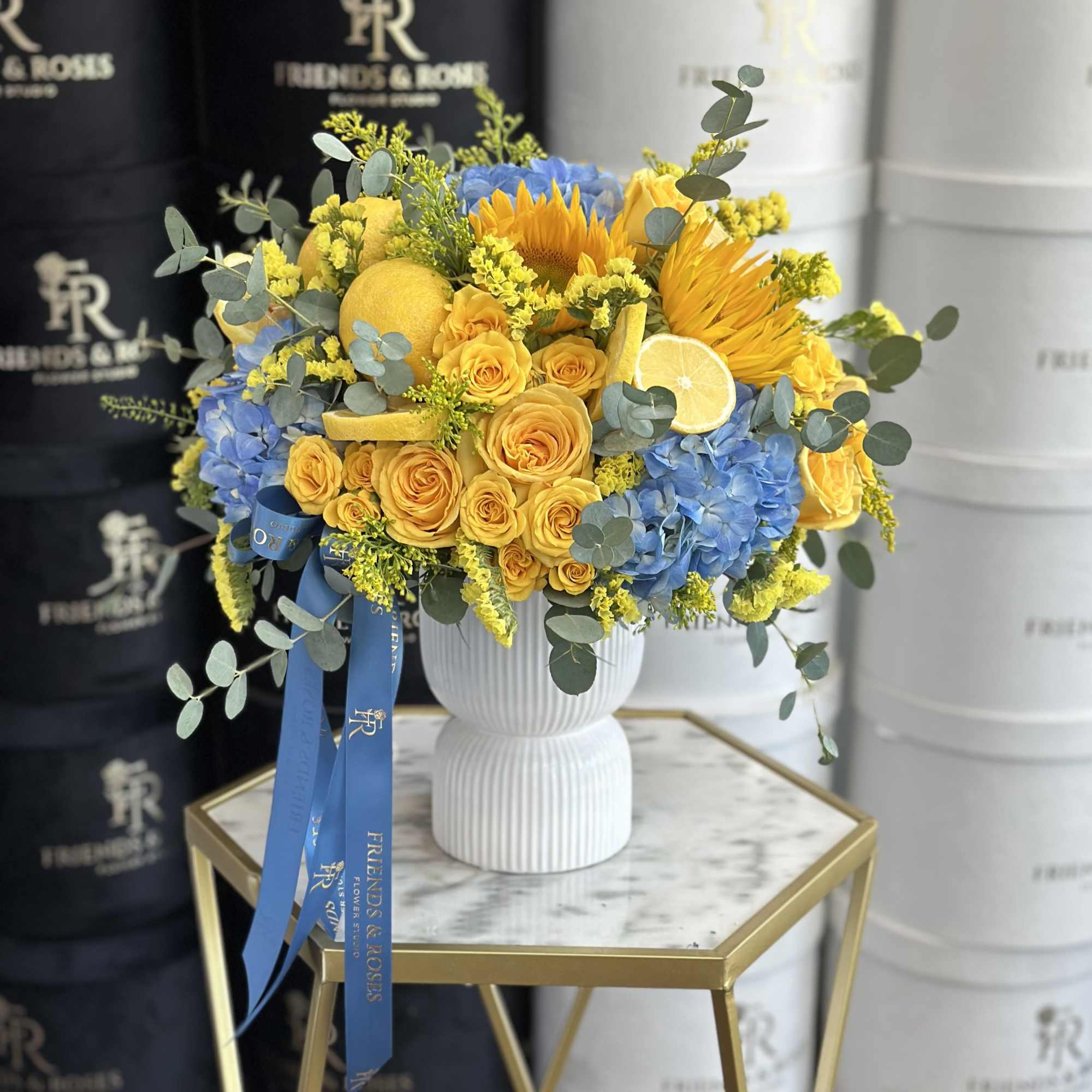 Yellow and blue flower arrangement in a white vase with ribbon