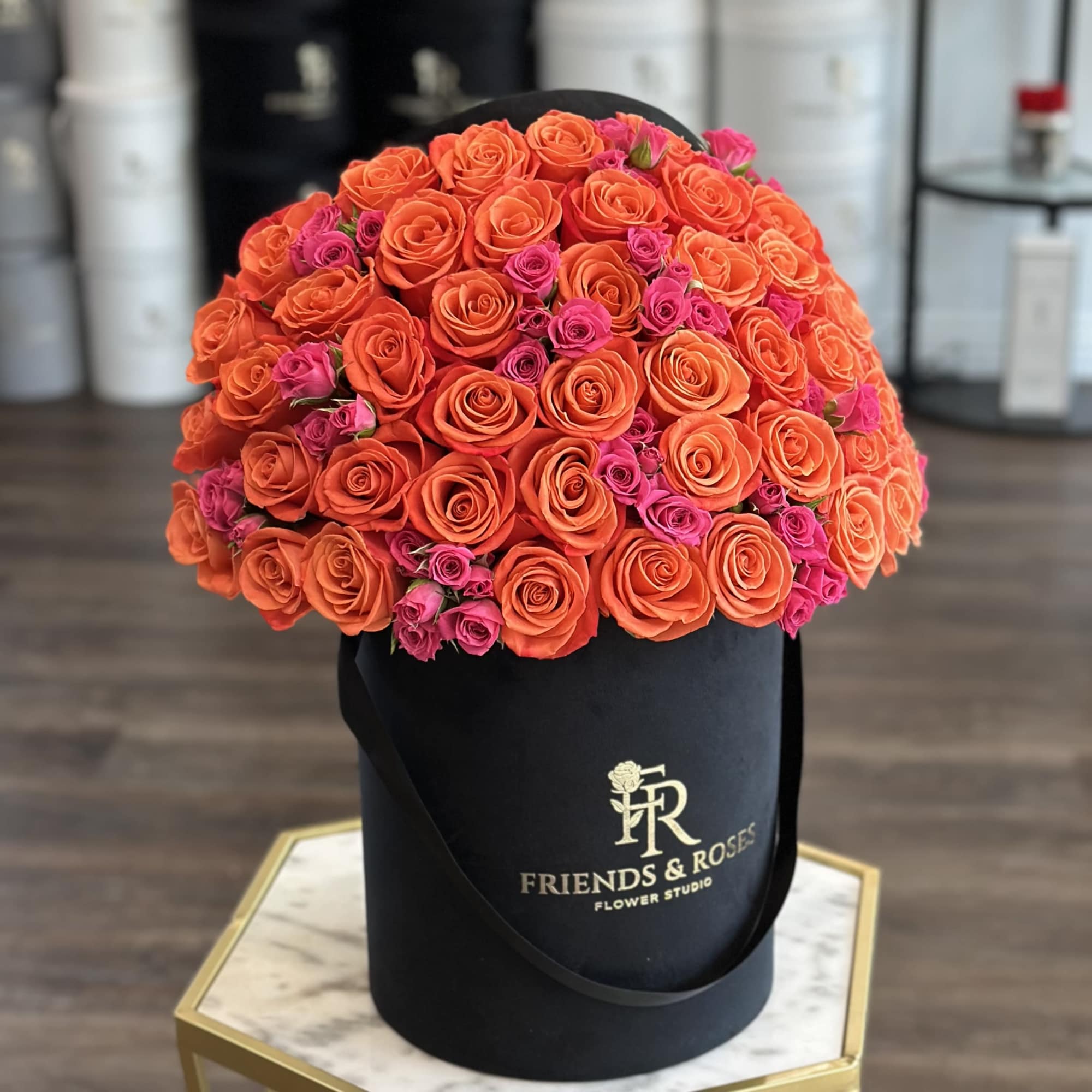 Orange and pink roses arranged in a black hat box