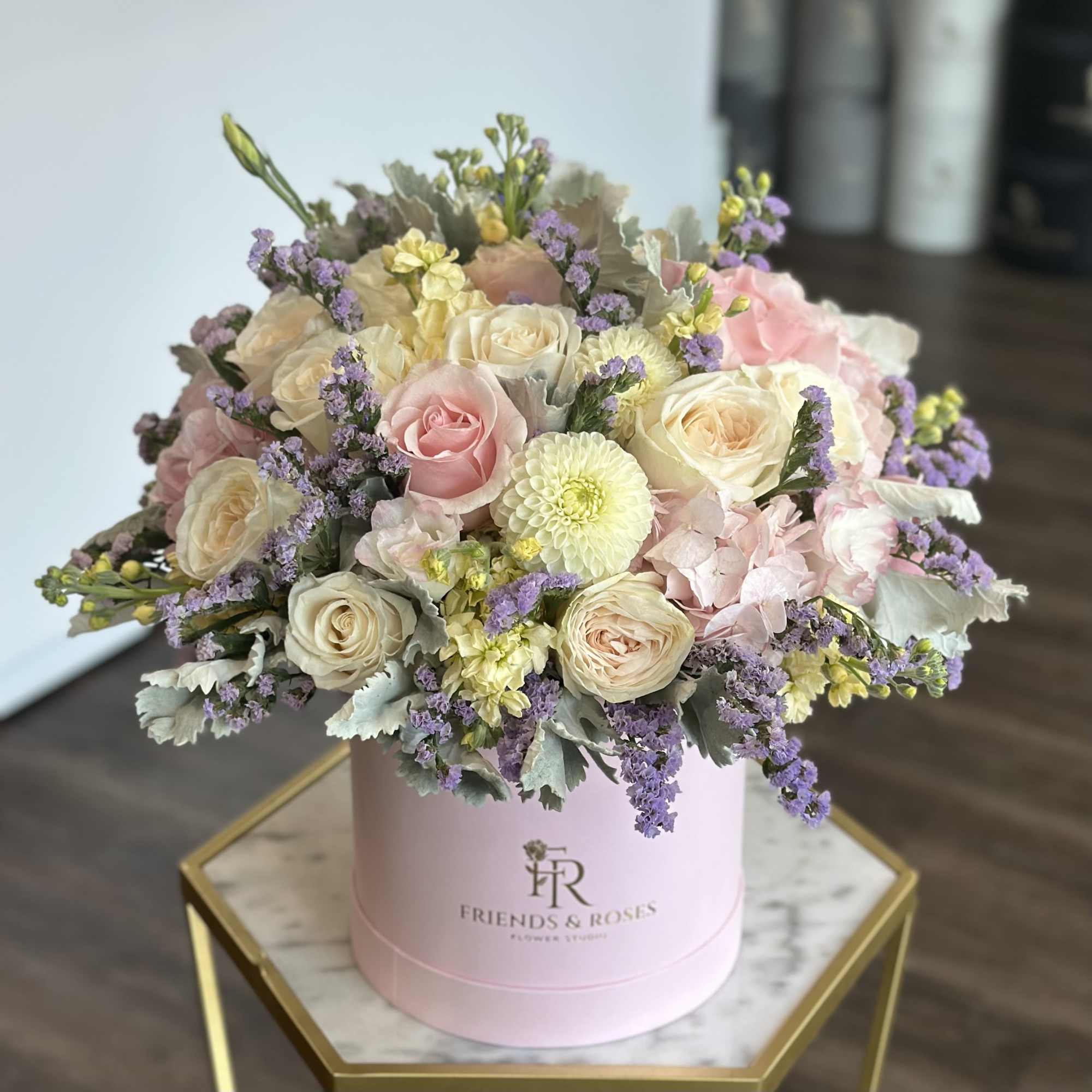 Pastel roses and small blooms arranged in a pink hat box