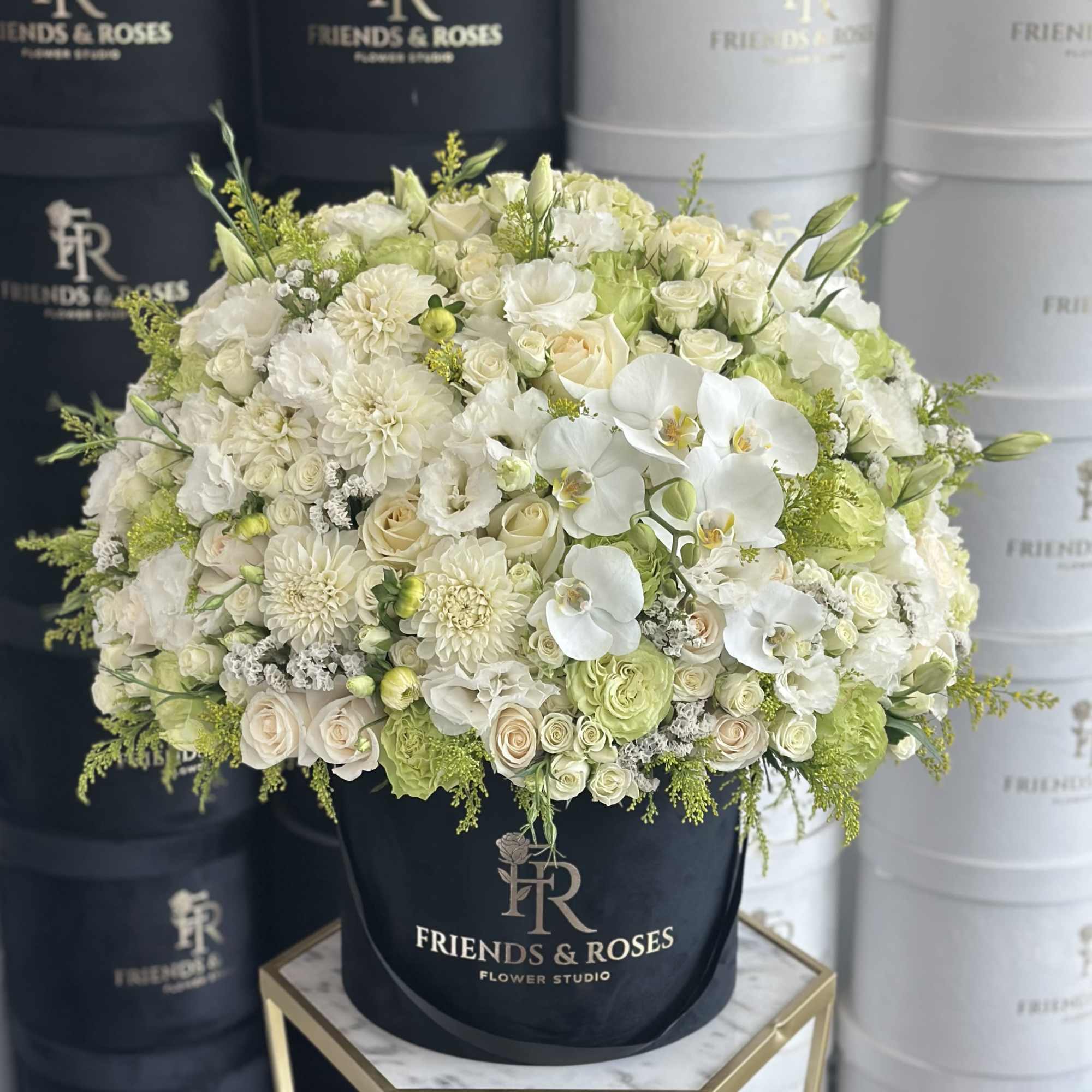 White and pale green floral arrangement in a black hatbox.