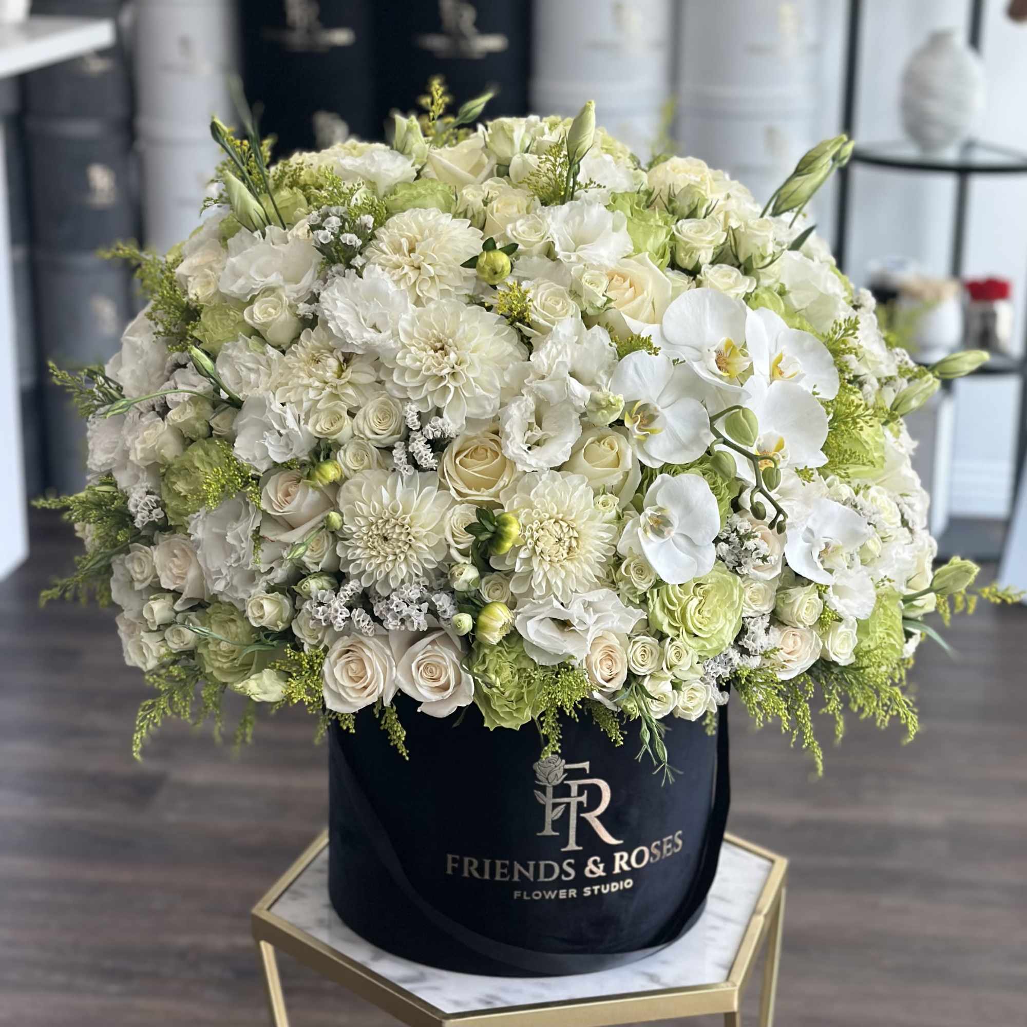 Large white floral arrangement in a black hatbox with orchids and roses