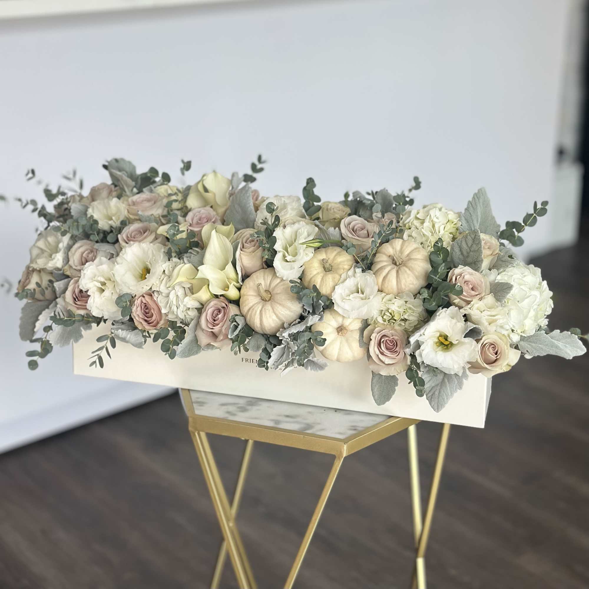 Low floral arrangement with pale roses, white blooms, and cream pumpkins in a white box