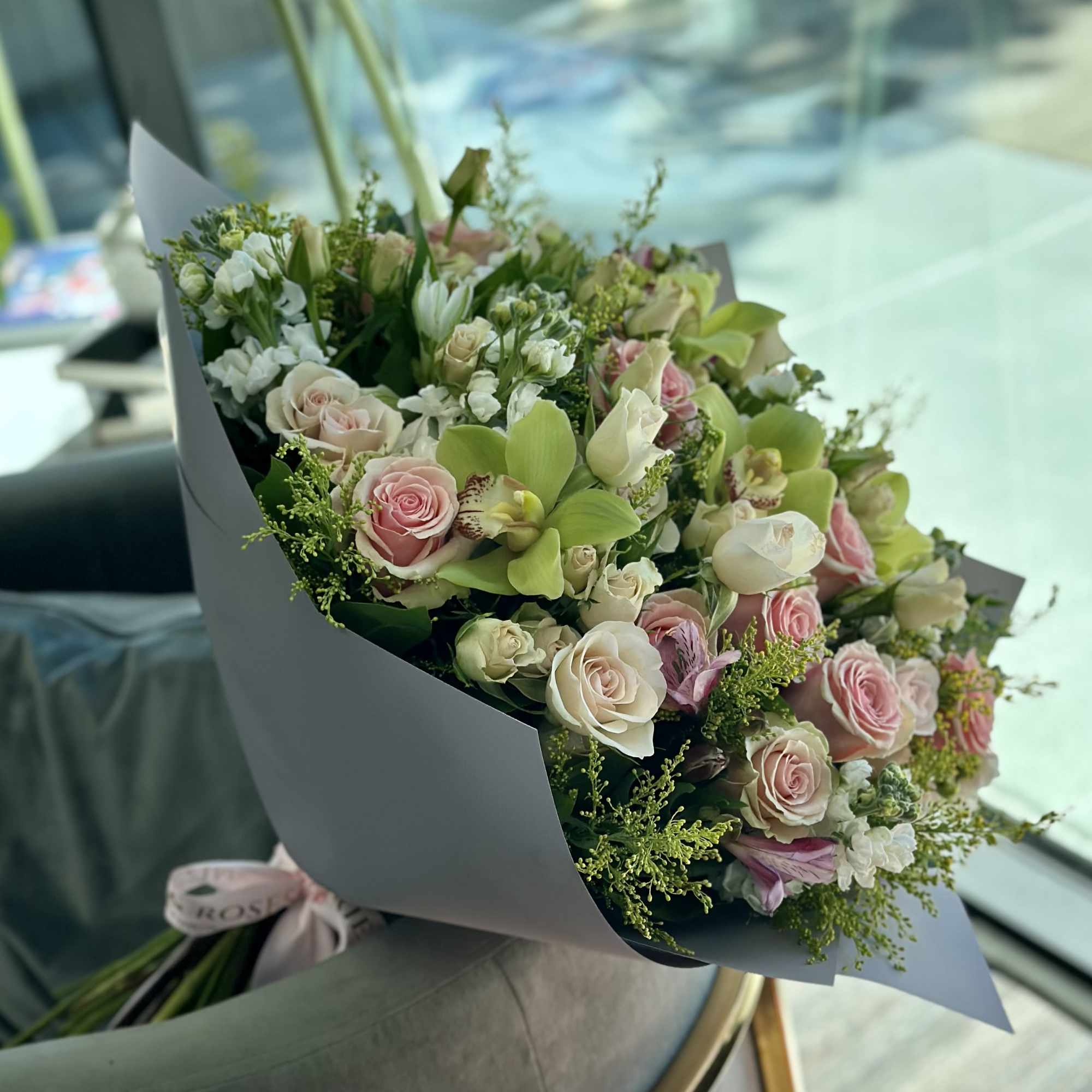 Bouquet of pink and white roses with green orchids wrapped in gray paper