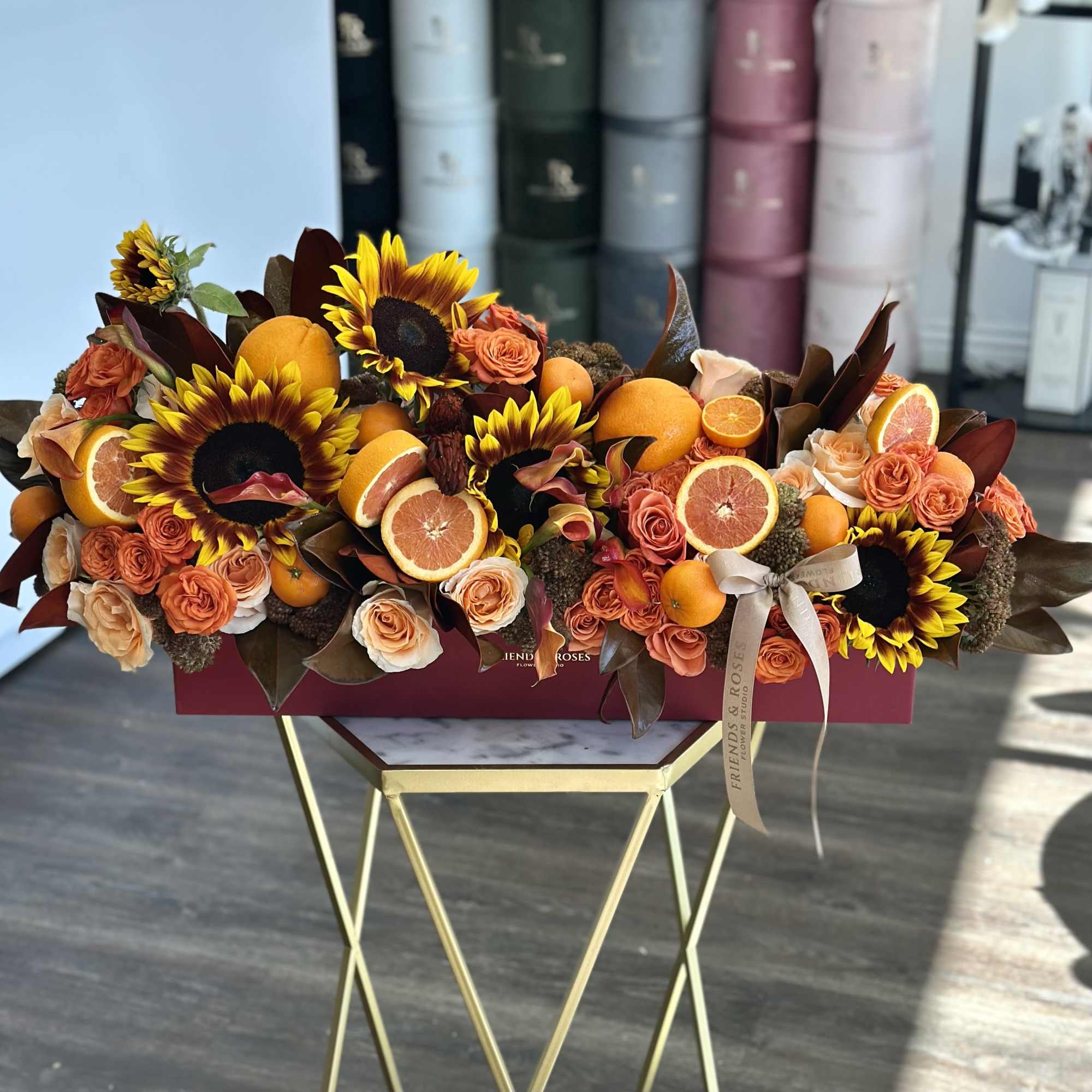 Sunflowers and orange roses arranged with sliced citrus in a rectangular box