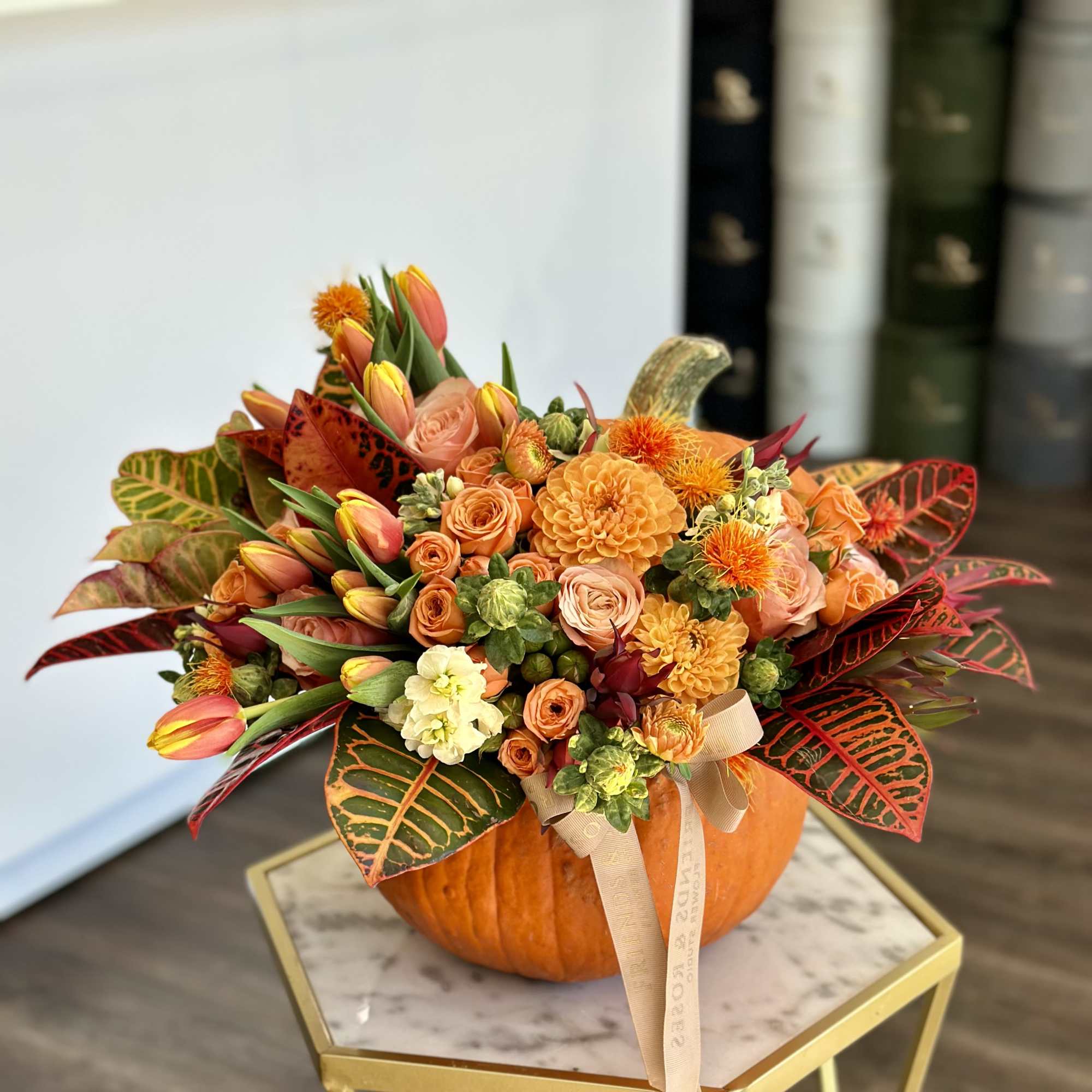Orange floral arrangement in a pumpkin container with ribbon