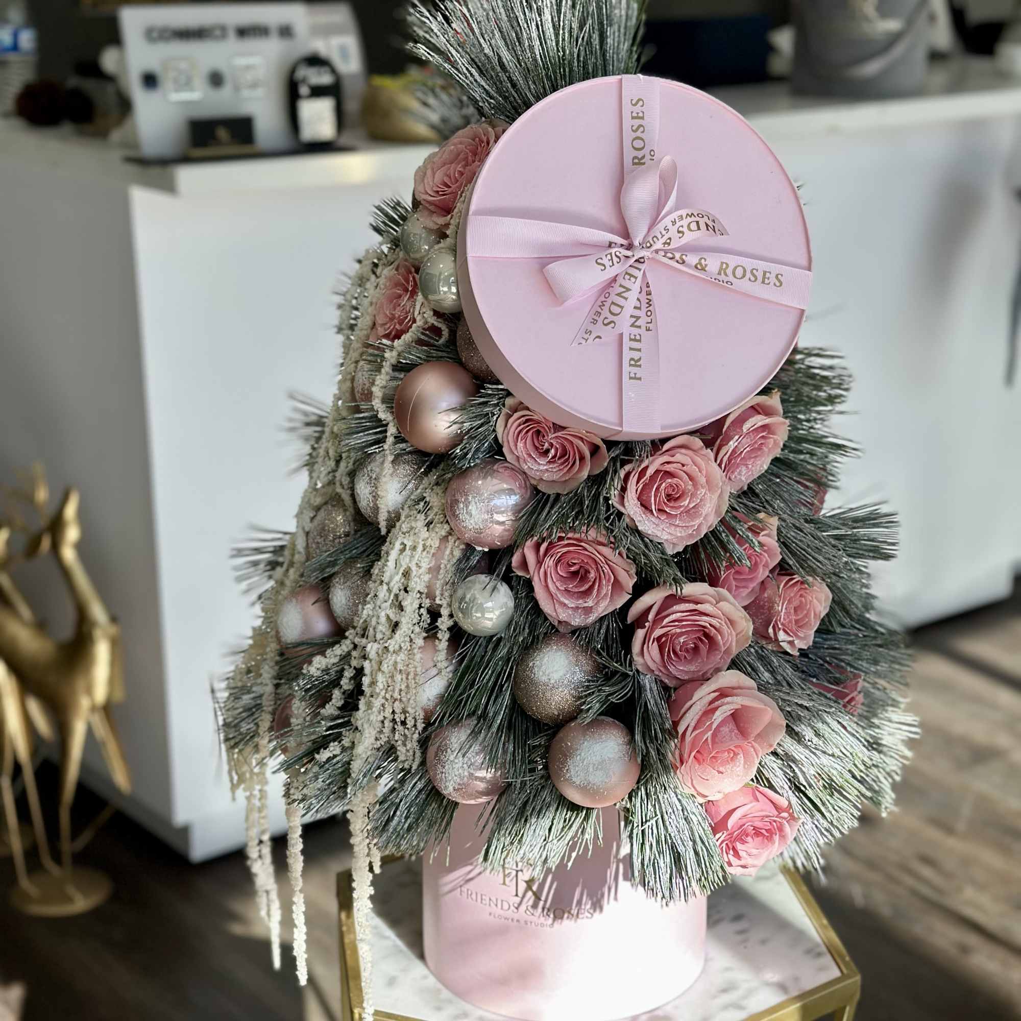Pink roses and ornaments arranged in a pink hat box with evergreen branches.