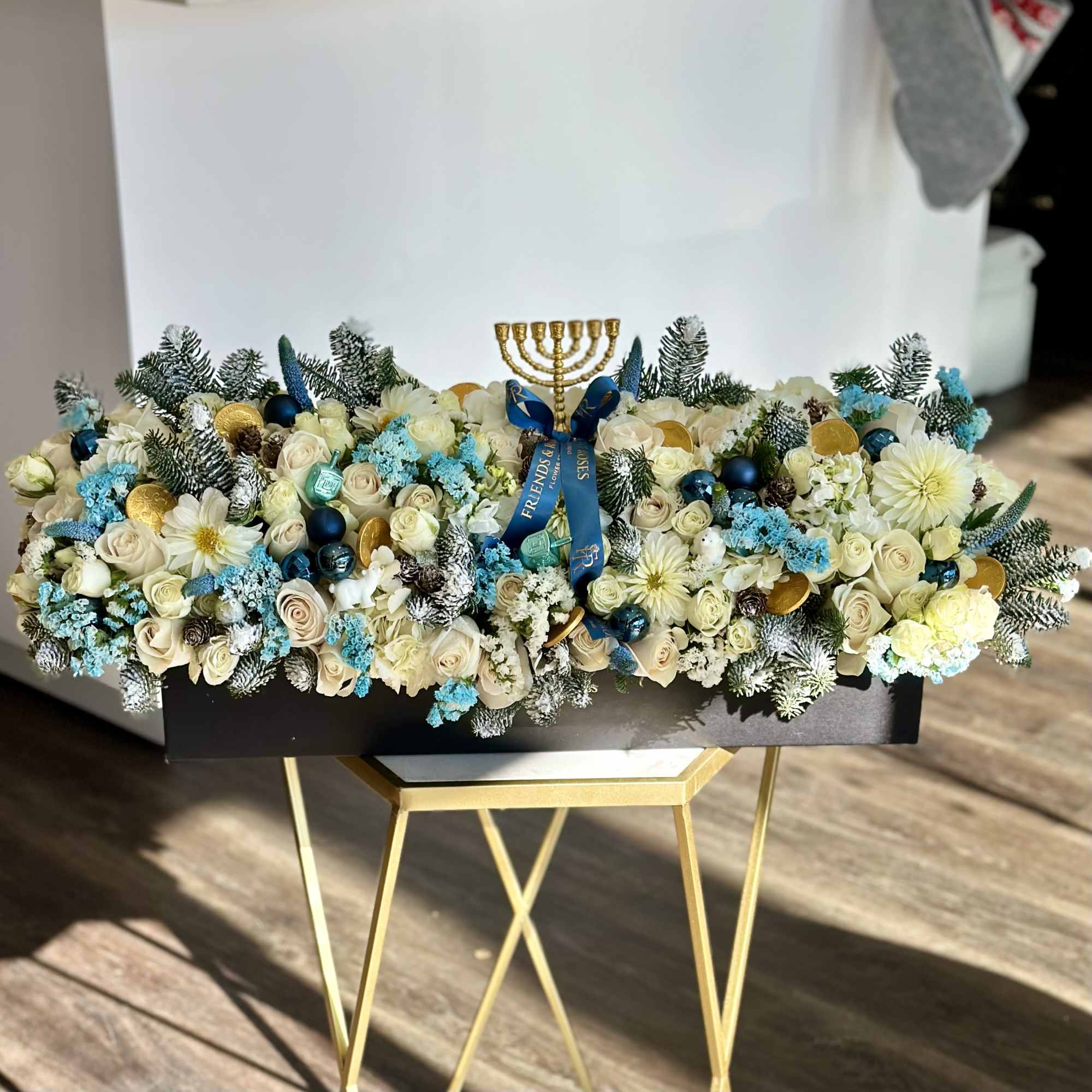 Long floral arrangement with cream roses, blue accents, and a gold menorah topper