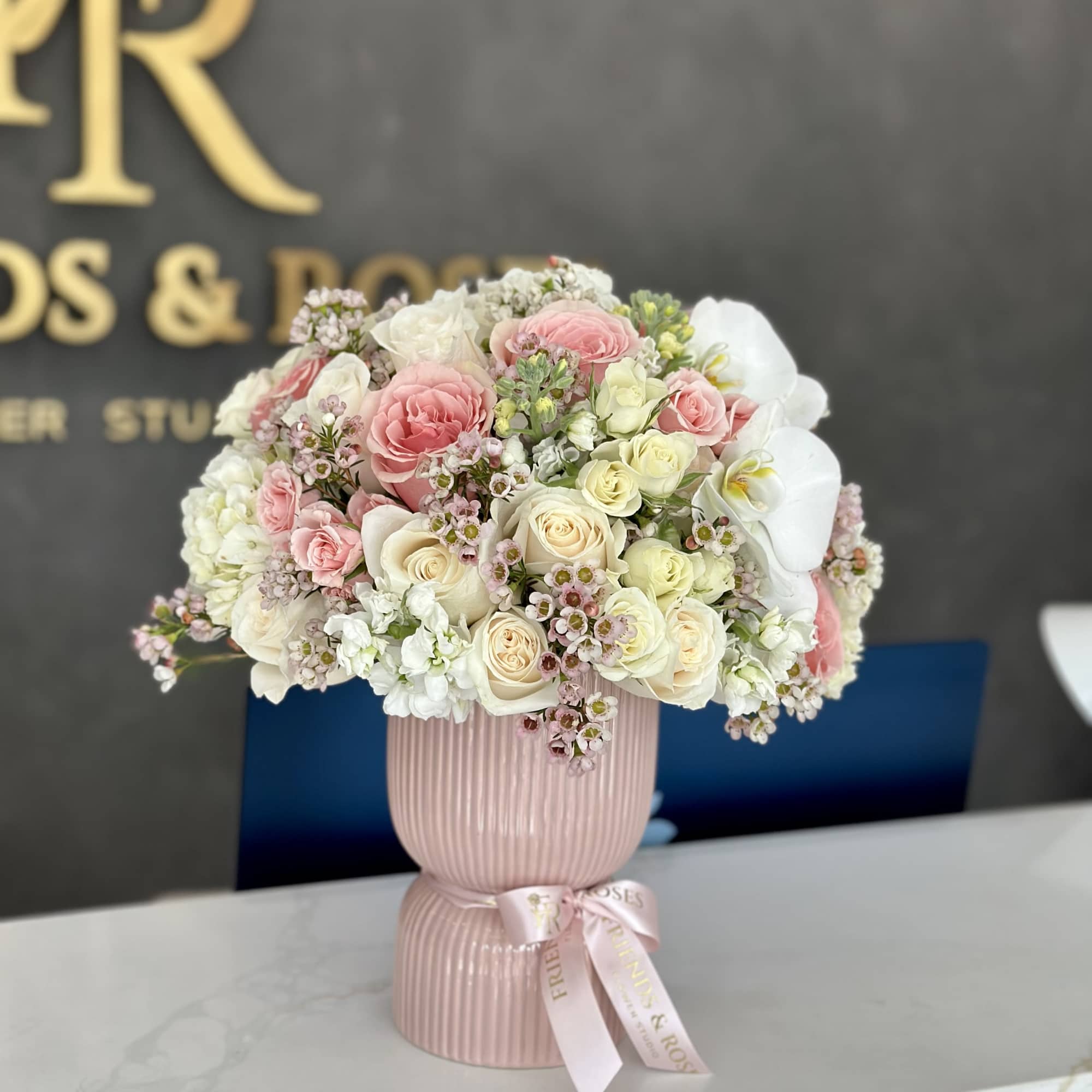 Pink and white rose bouquet in a ribbed pink vase with a ribbon