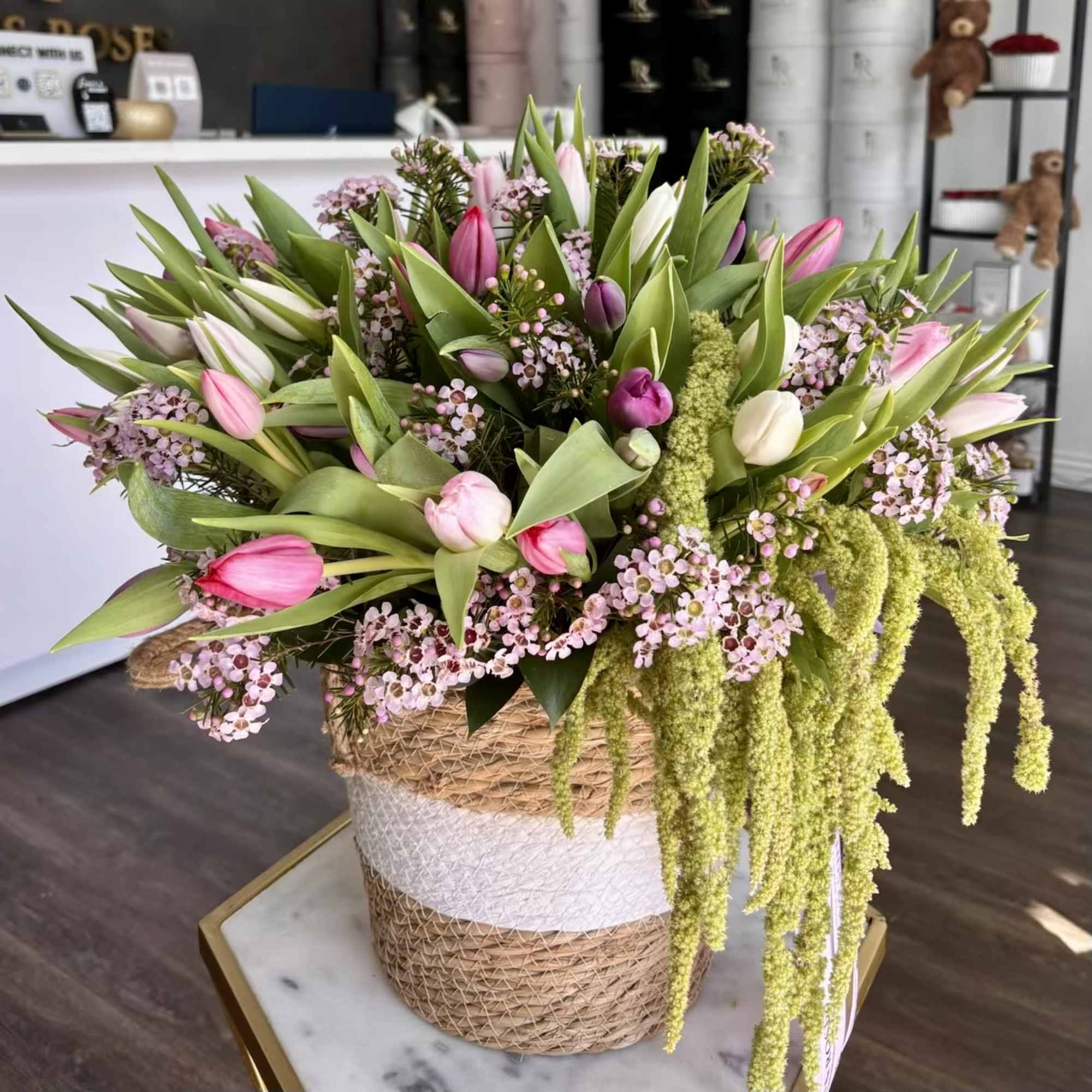 Large bouquet of pink and white tulips with trailing green blooms in a woven basket.