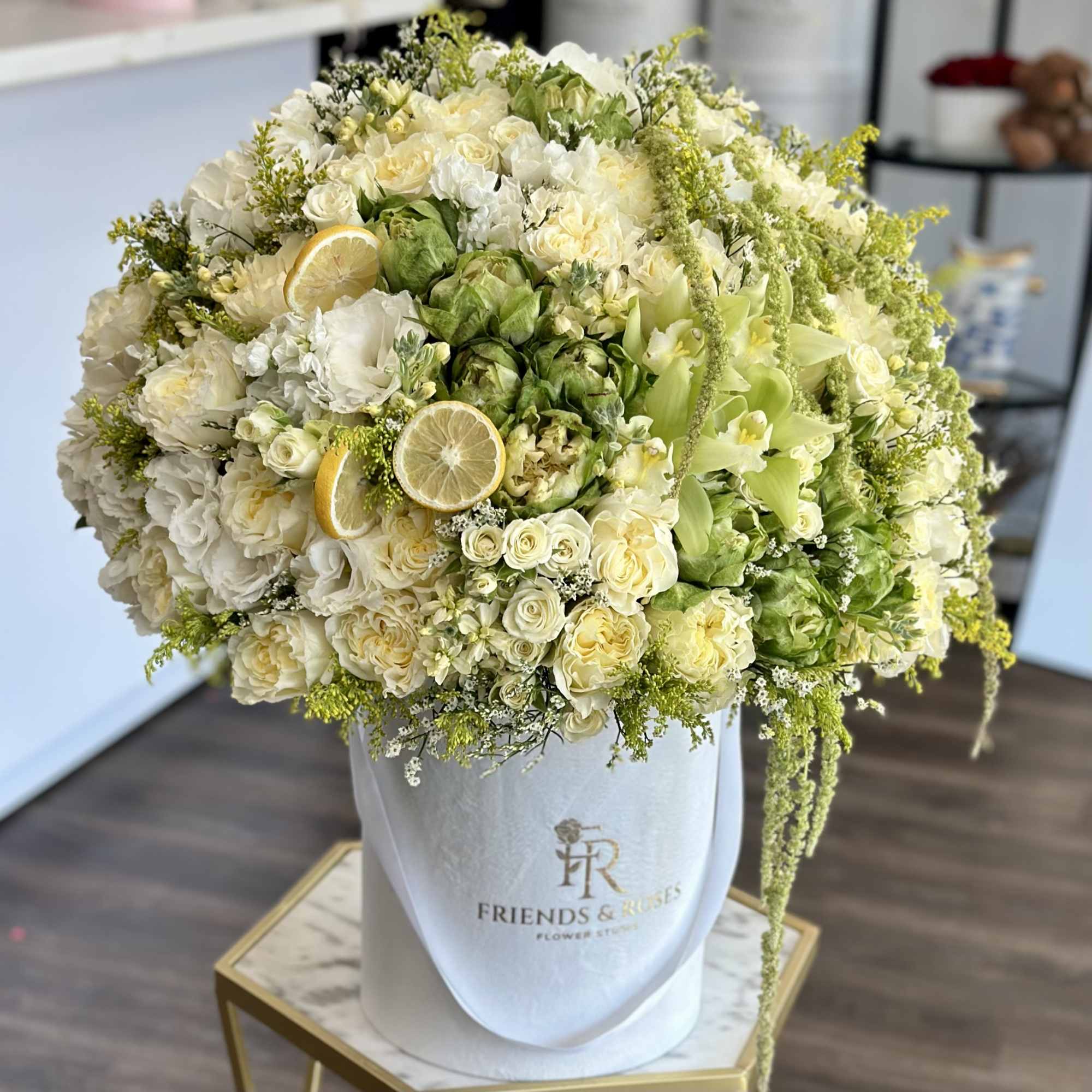 Large white and pale green floral arrangement in a white hatbox with lemon slices