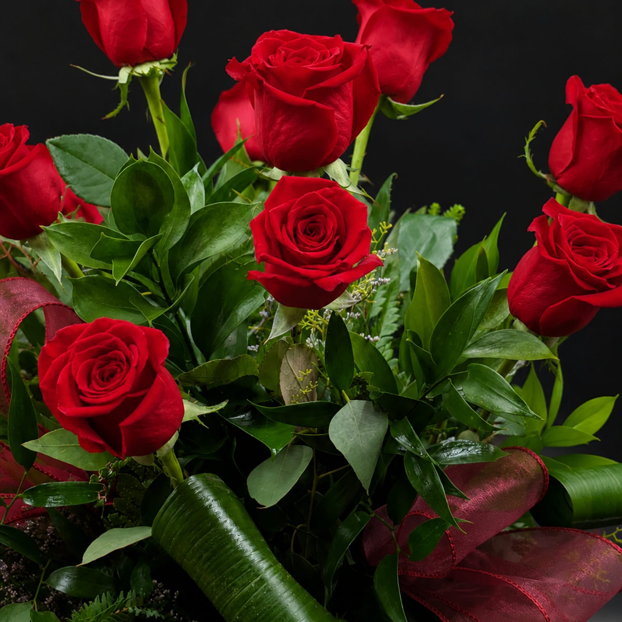 Bouquet of red roses with glossy greenery and burgundy ribbon on a black background