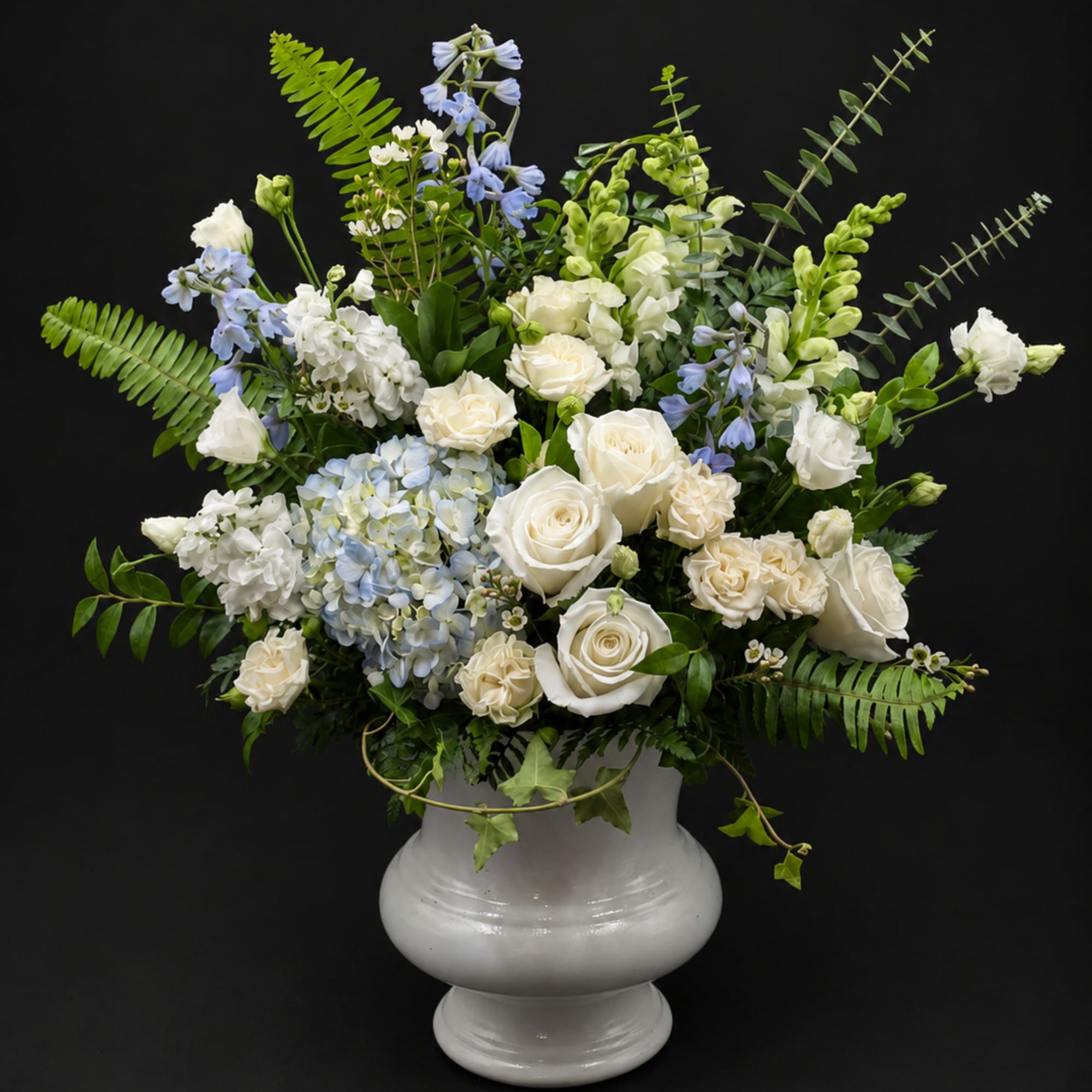 White roses and blue flowers arranged in a white urn vase