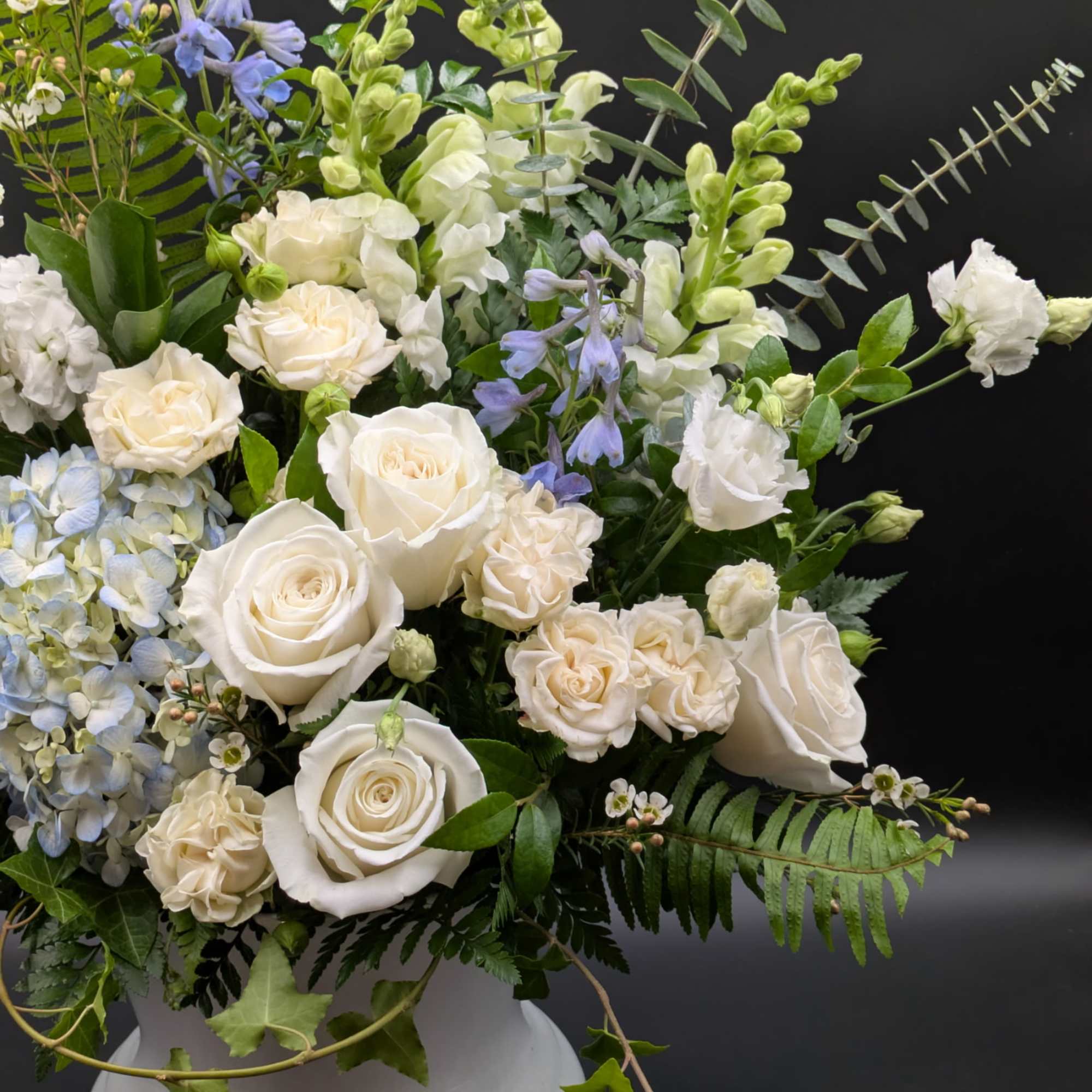 White roses and blue flowers arranged in a white vase