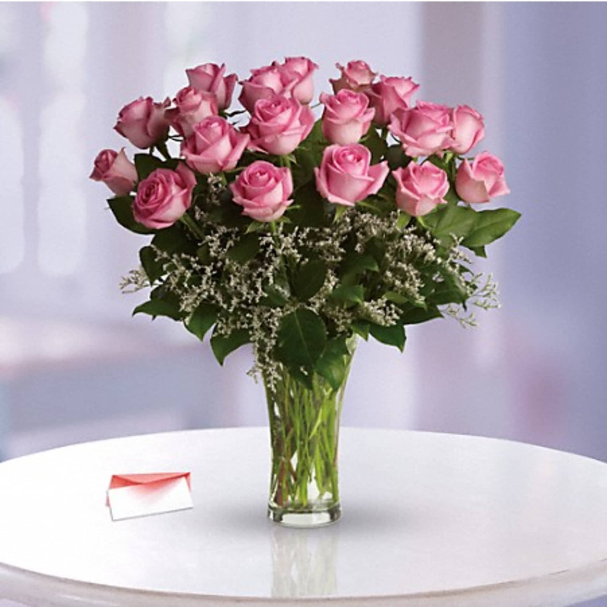 Pink roses arranged in a clear glass vase with a small card