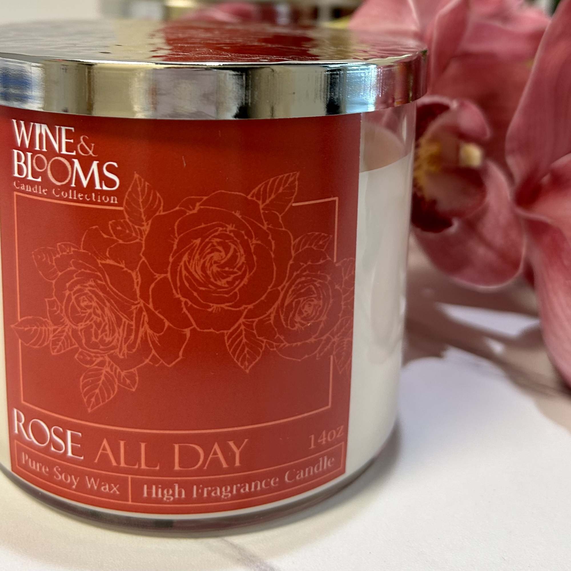 Rose-scented candle in a glass jar beside pink flowers