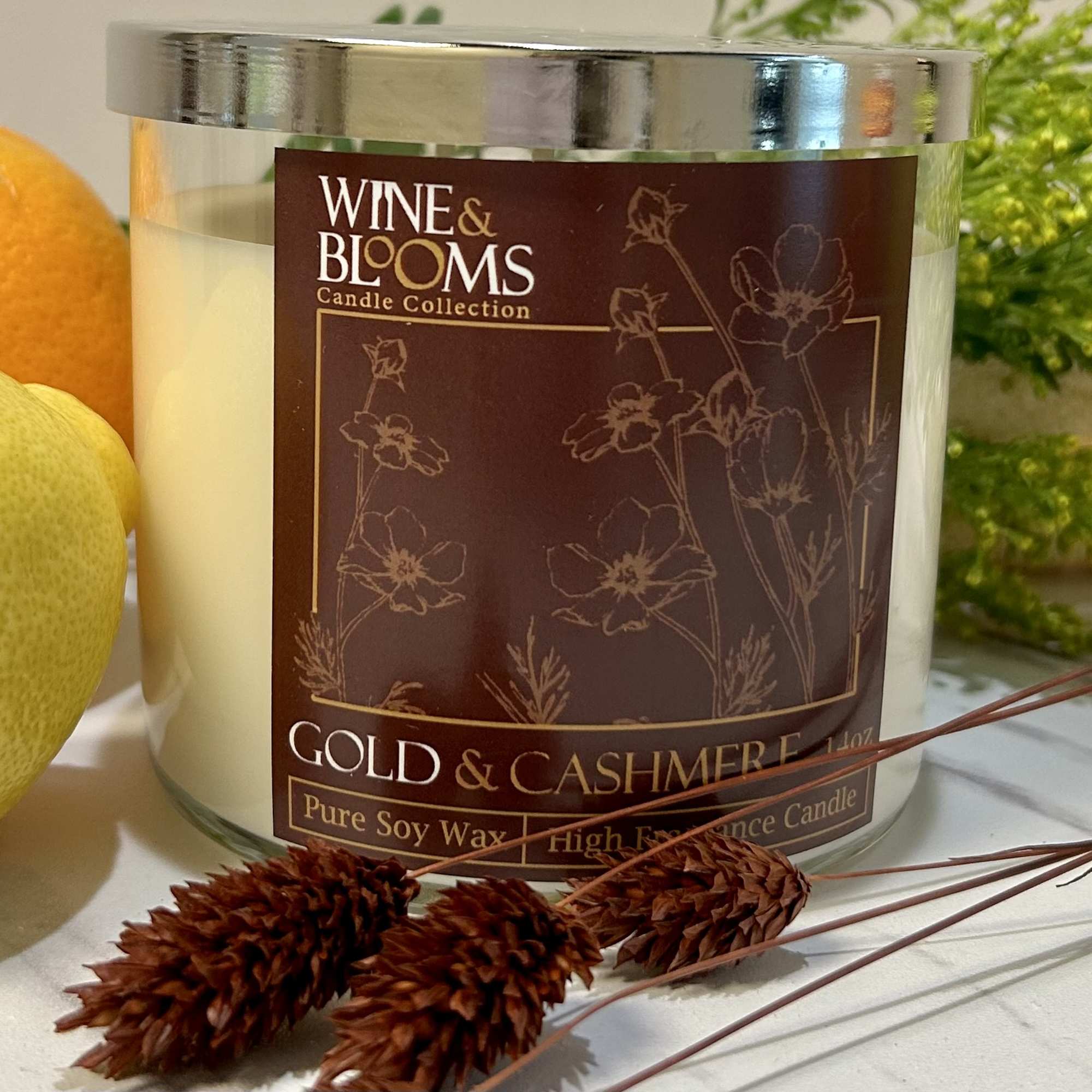 Scented candle in a glass jar beside oranges and dried stems