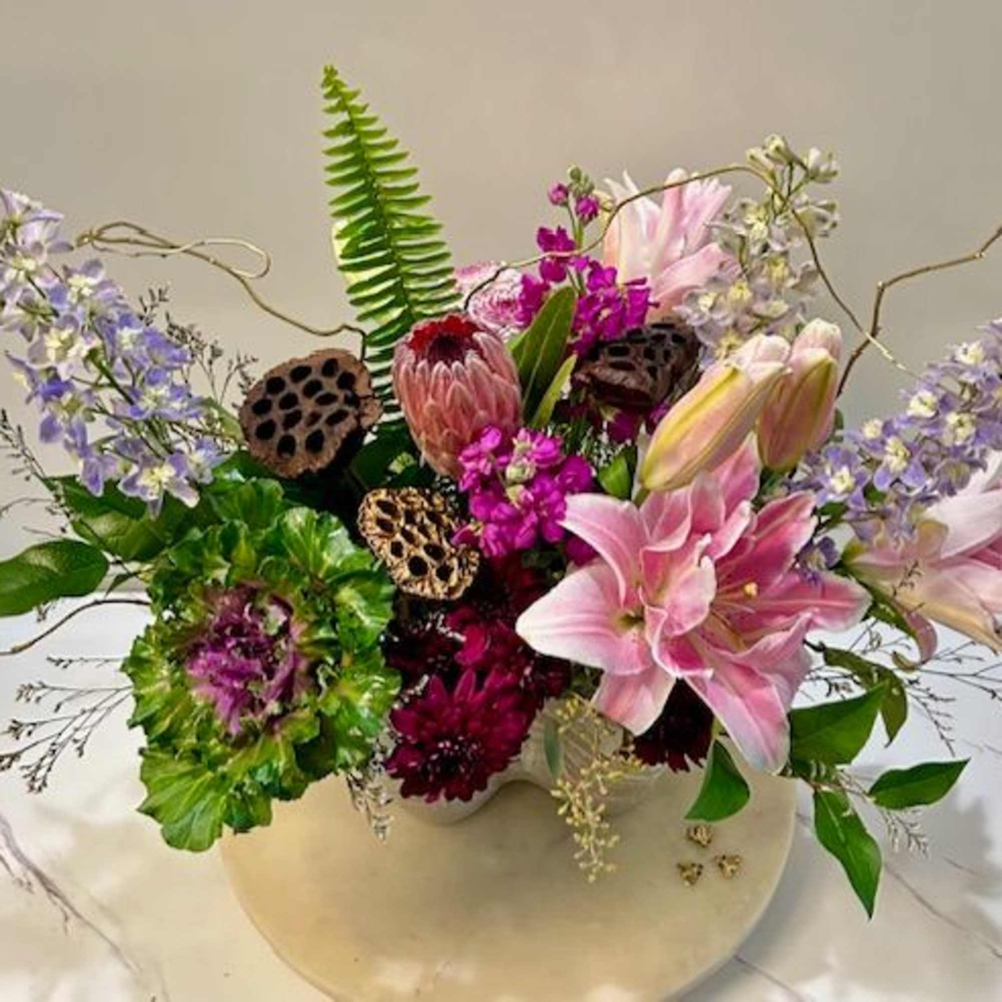 Mixed bouquet with pink lilies, purple blooms, and a white vase