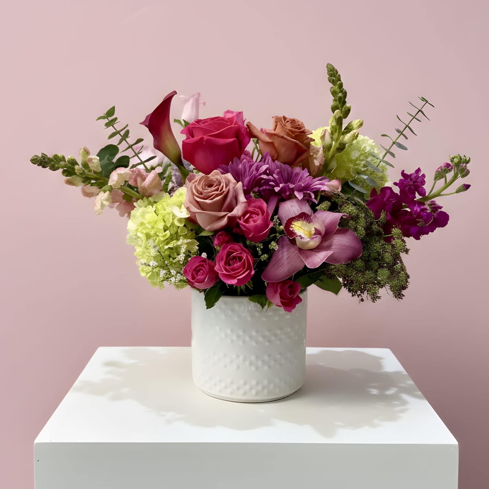 Mixed bouquet of pink, purple, and green flowers in a white vase