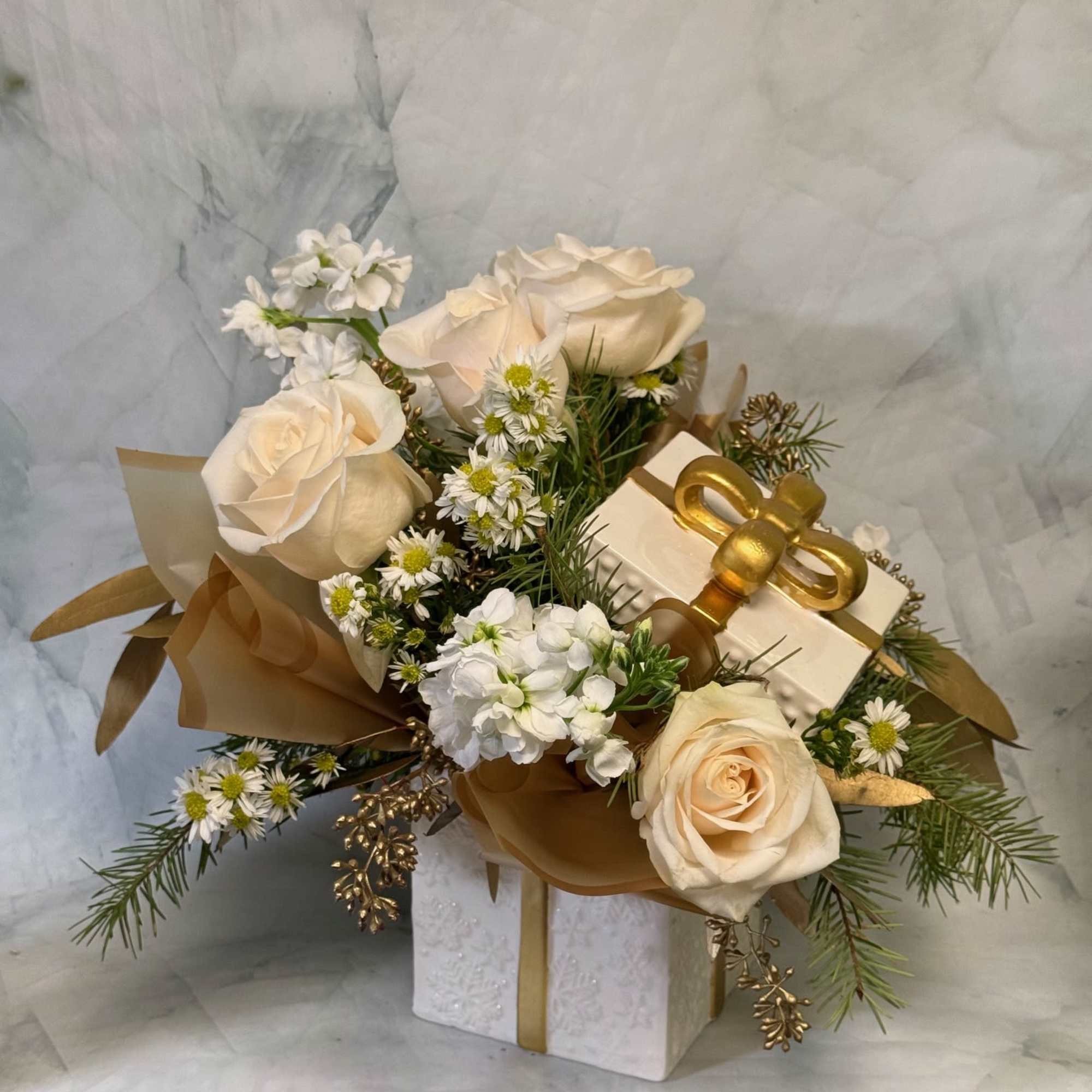 Cream roses and small white flowers arranged with a gift box and gold ribbon