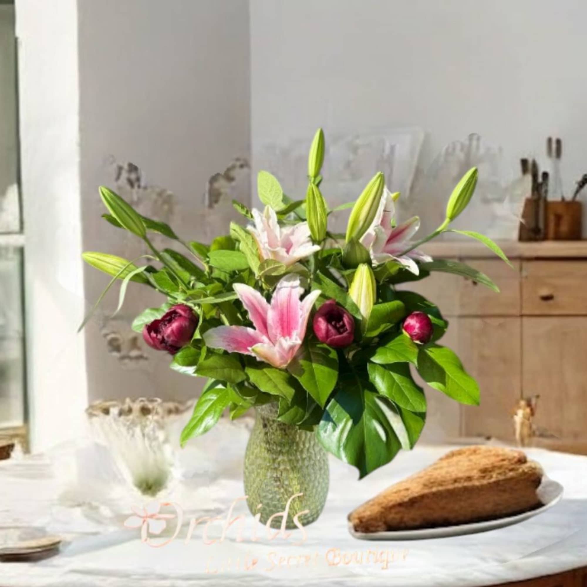 Pink lilies in a glass vase on a table with a loaf of bread