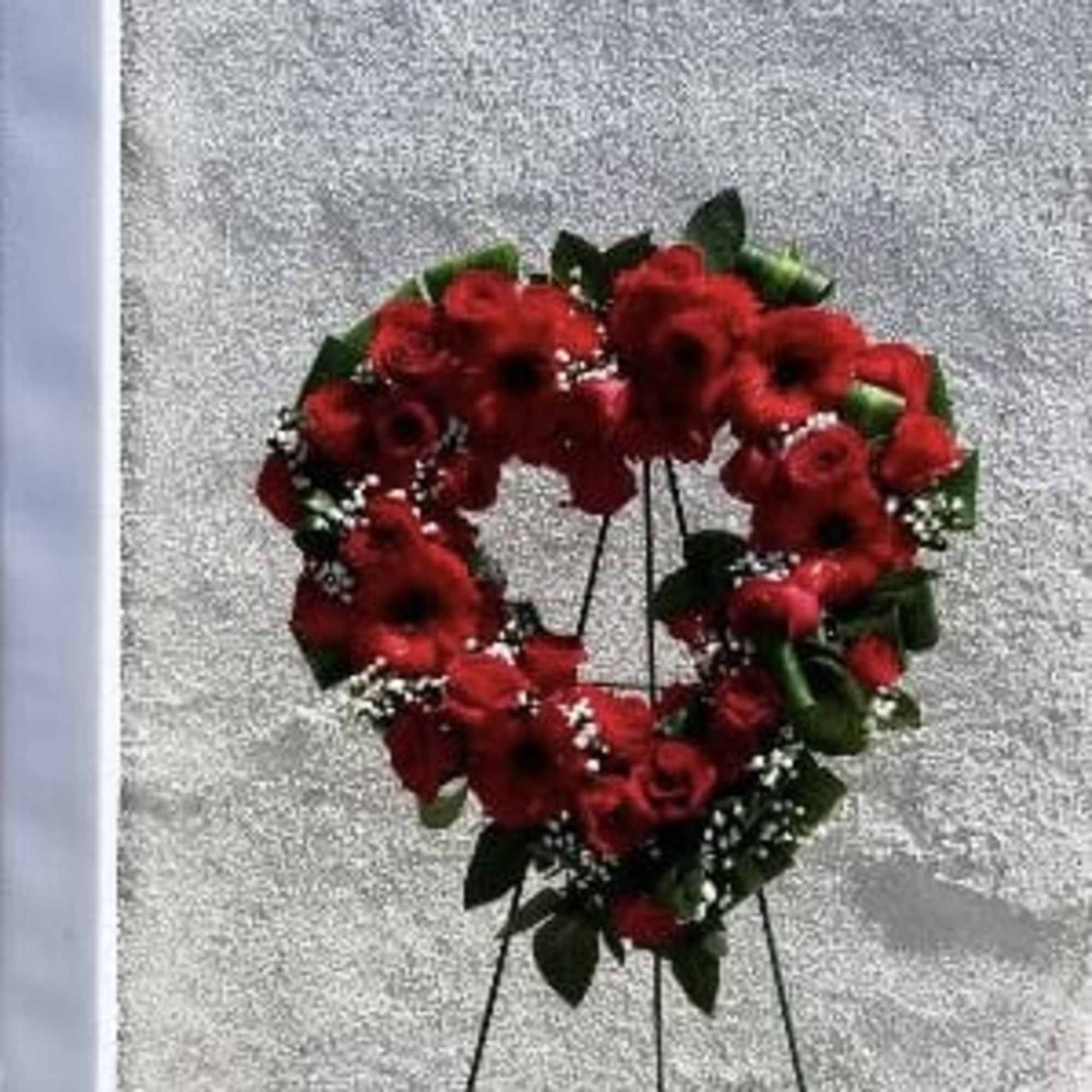 Heart-shaped red floral wreath on a black stand