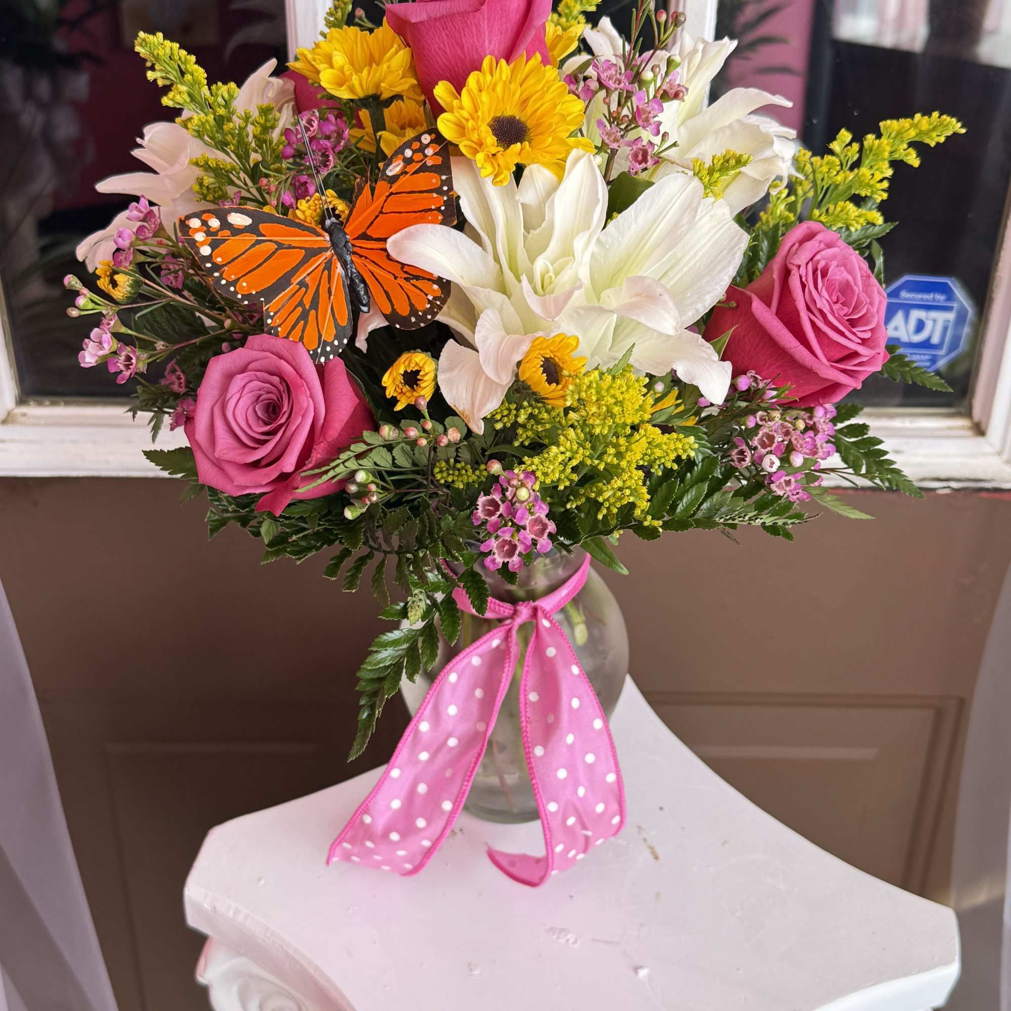 Pink roses and white lilies in a glass vase with a butterfly accent