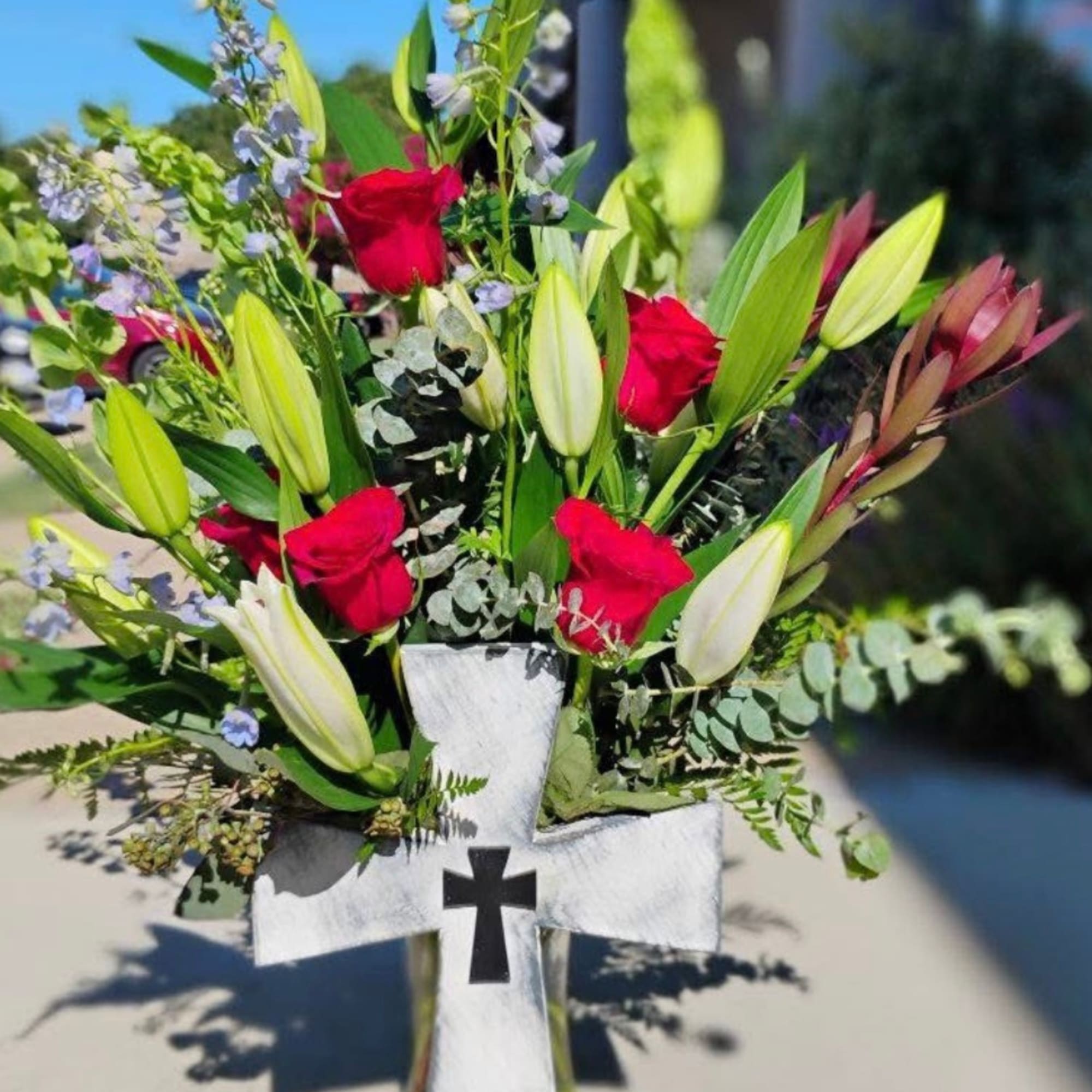 Red roses and white lilies arranged in a white cross-shaped stand