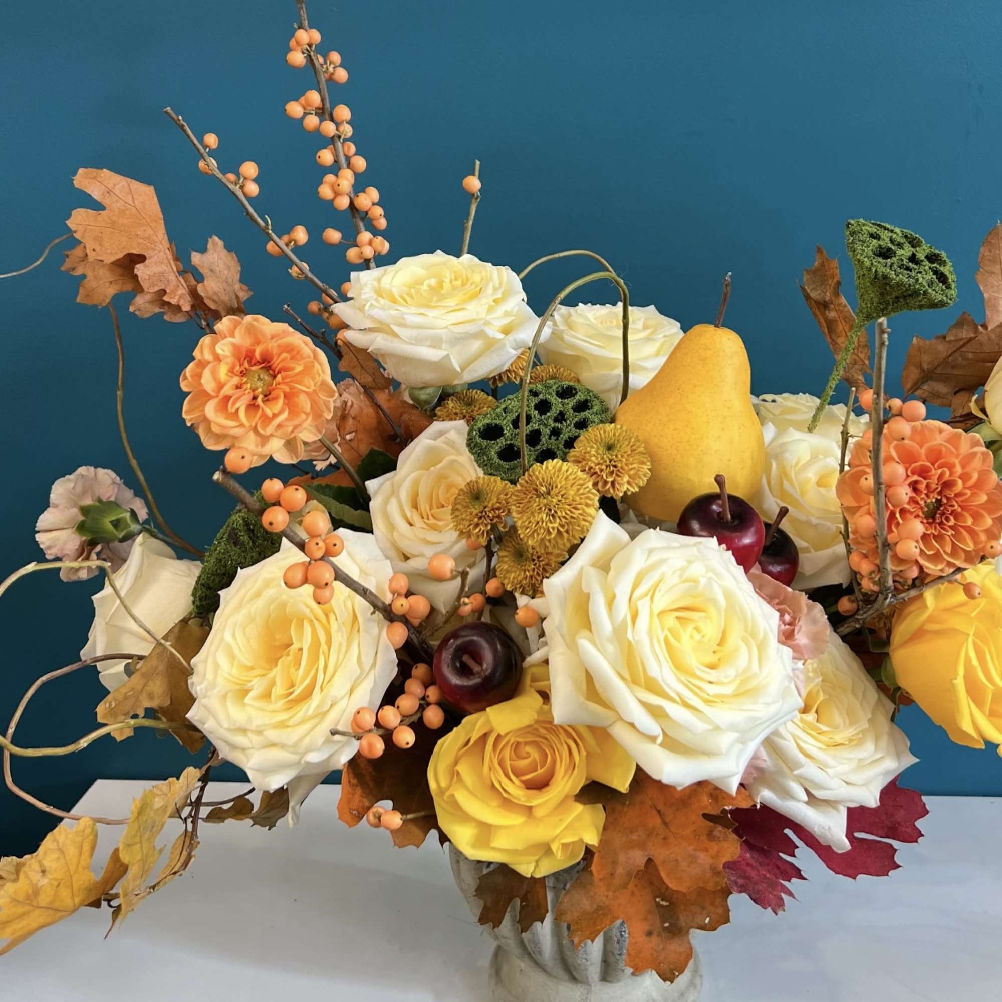 Arrangement of cream and yellow roses with autumn berries and leaves in a vase