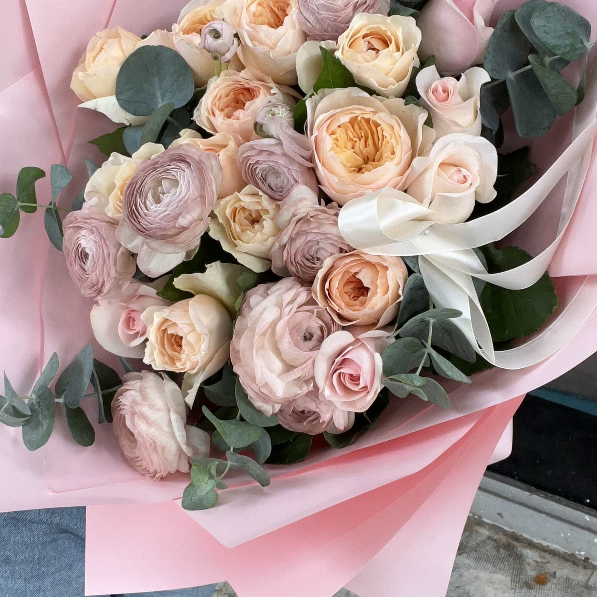 Bouquet of blush and peach roses with eucalyptus wrapped in pink paper