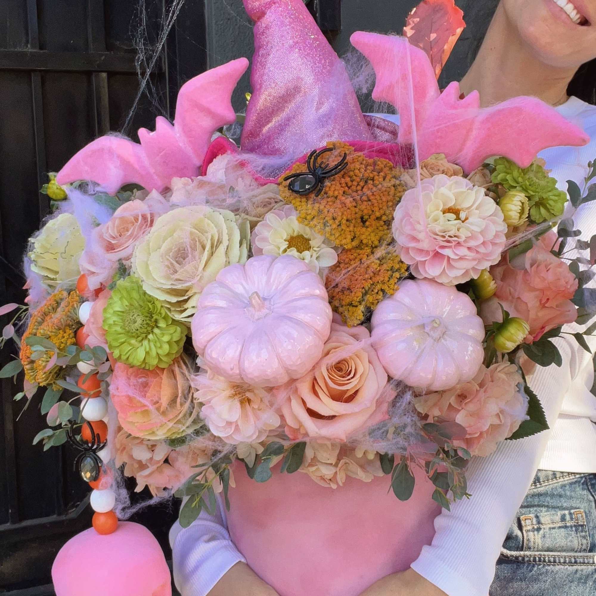 Pink pumpkin-shaped floral arrangement with roses, dahlias, and Halloween decorations