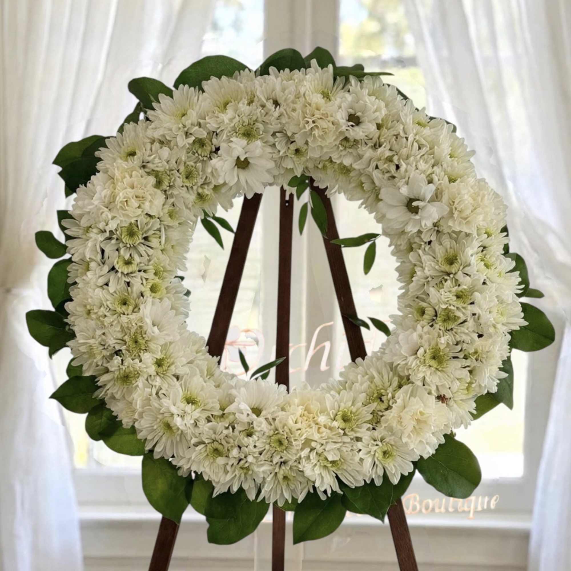 White flower wreath on a wooden easel with green leaves
