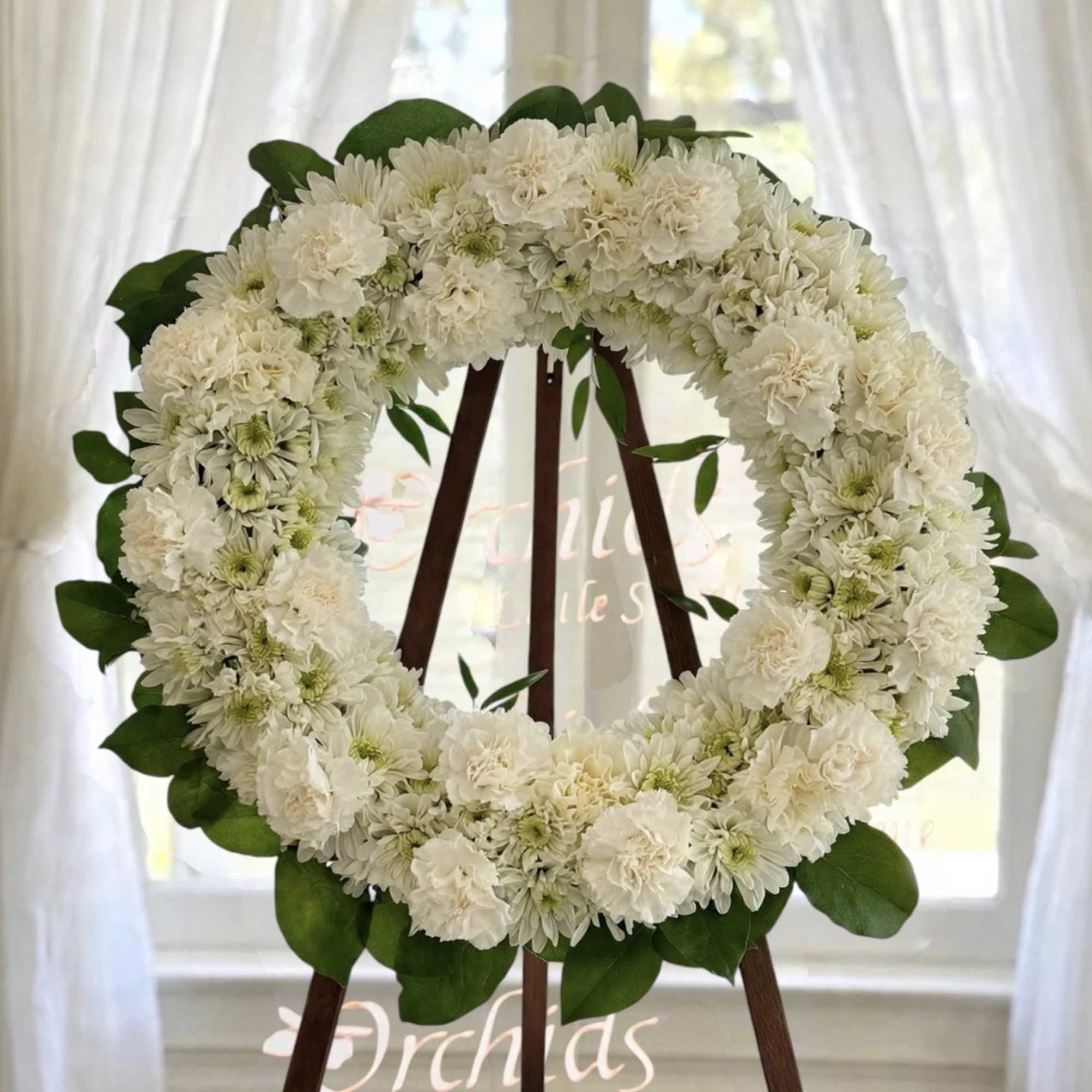 White floral wreath on a wooden easel with green leaves