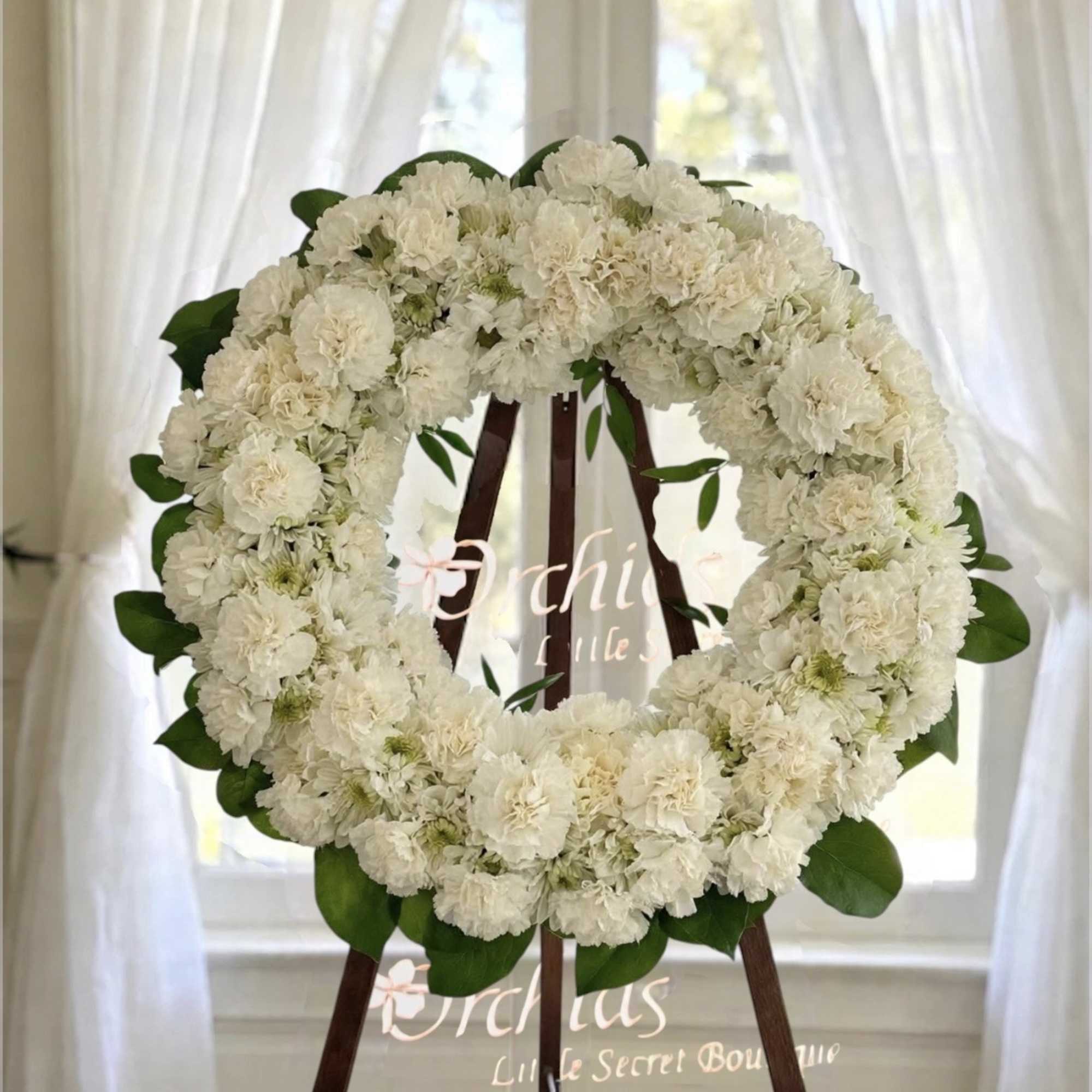 White floral wreath on a wooden easel with green leaves