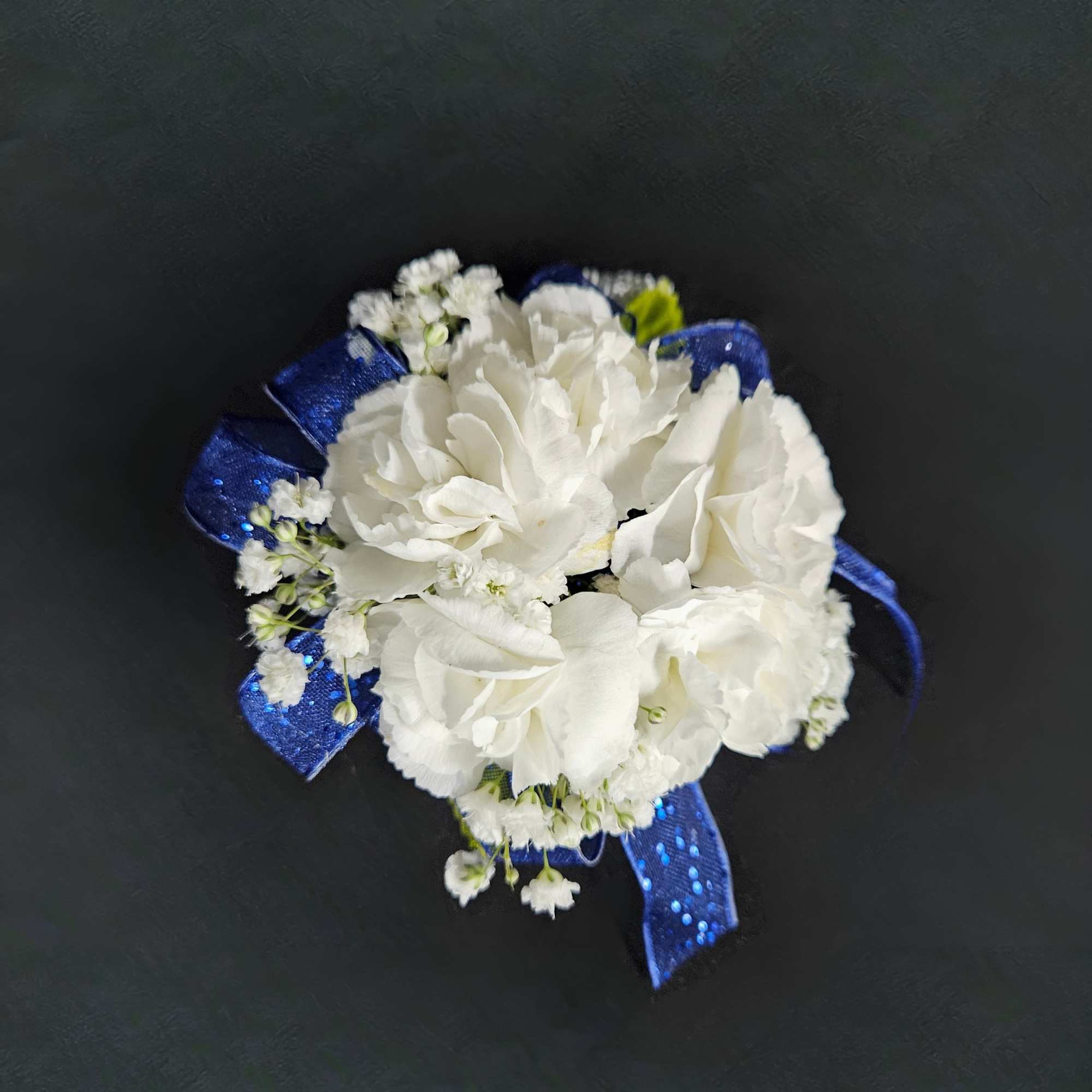 White floral corsage with blue ribbon on a dark background