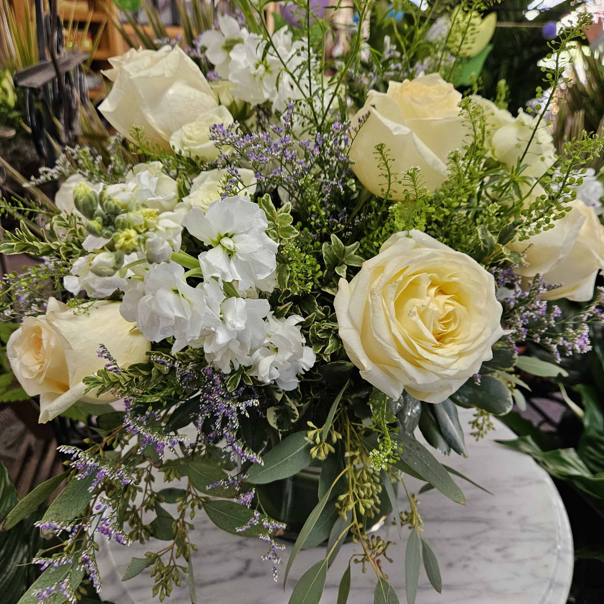 Vase of cream roses, white blooms, and delicate lavender accents in a lush round arrangement