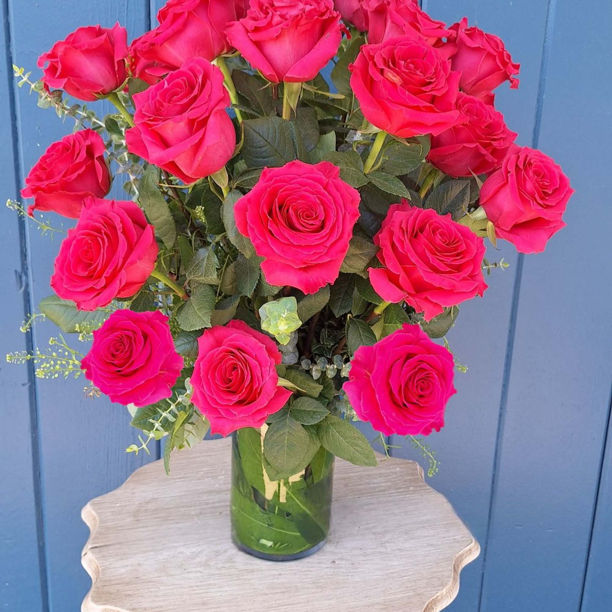 Tall arrangement of bright pink roses in a clear glass vase on a small table