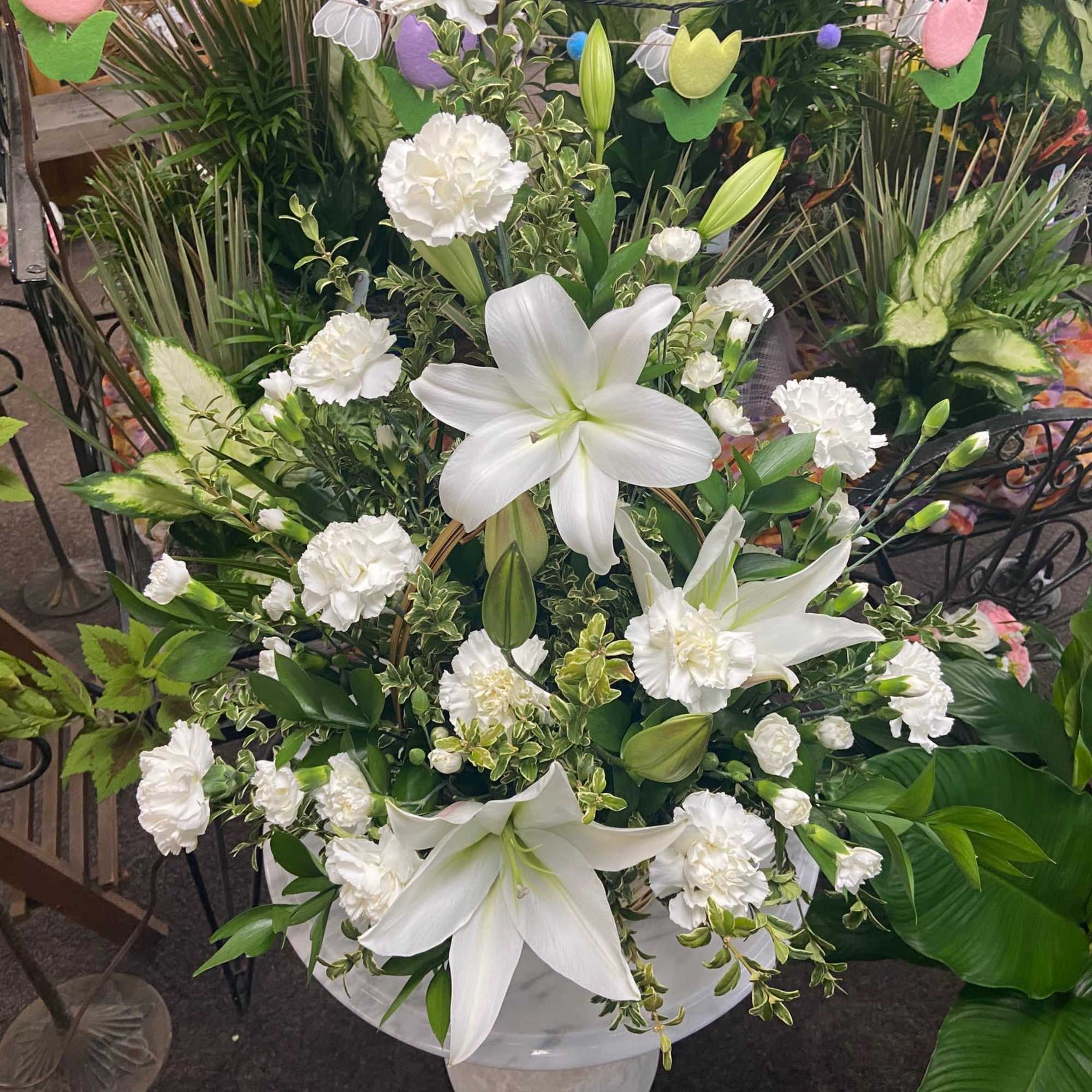 Tall arrangement of white lilies and white carnations in a white urn-style container