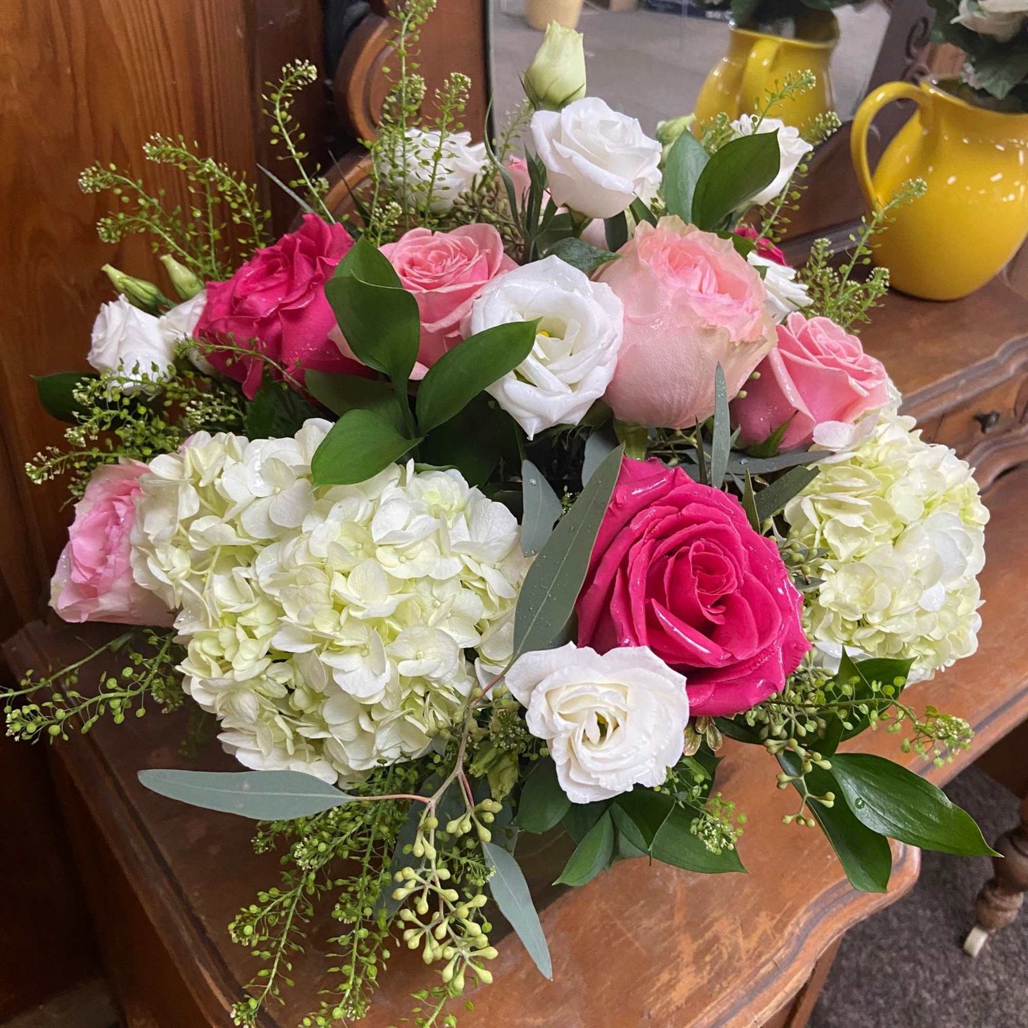 Low arrangement of pink and white roses with white hydrangeas on a wooden table