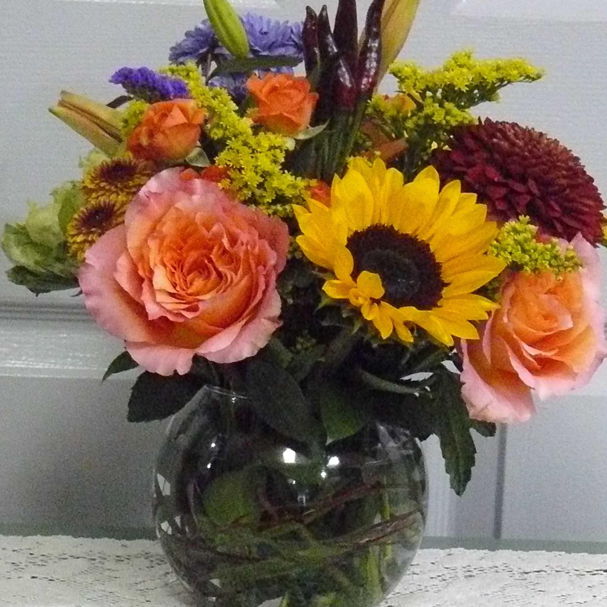 Mixed bouquet of roses, sunflowers, lilies, and chrysanthemums in a glass vase