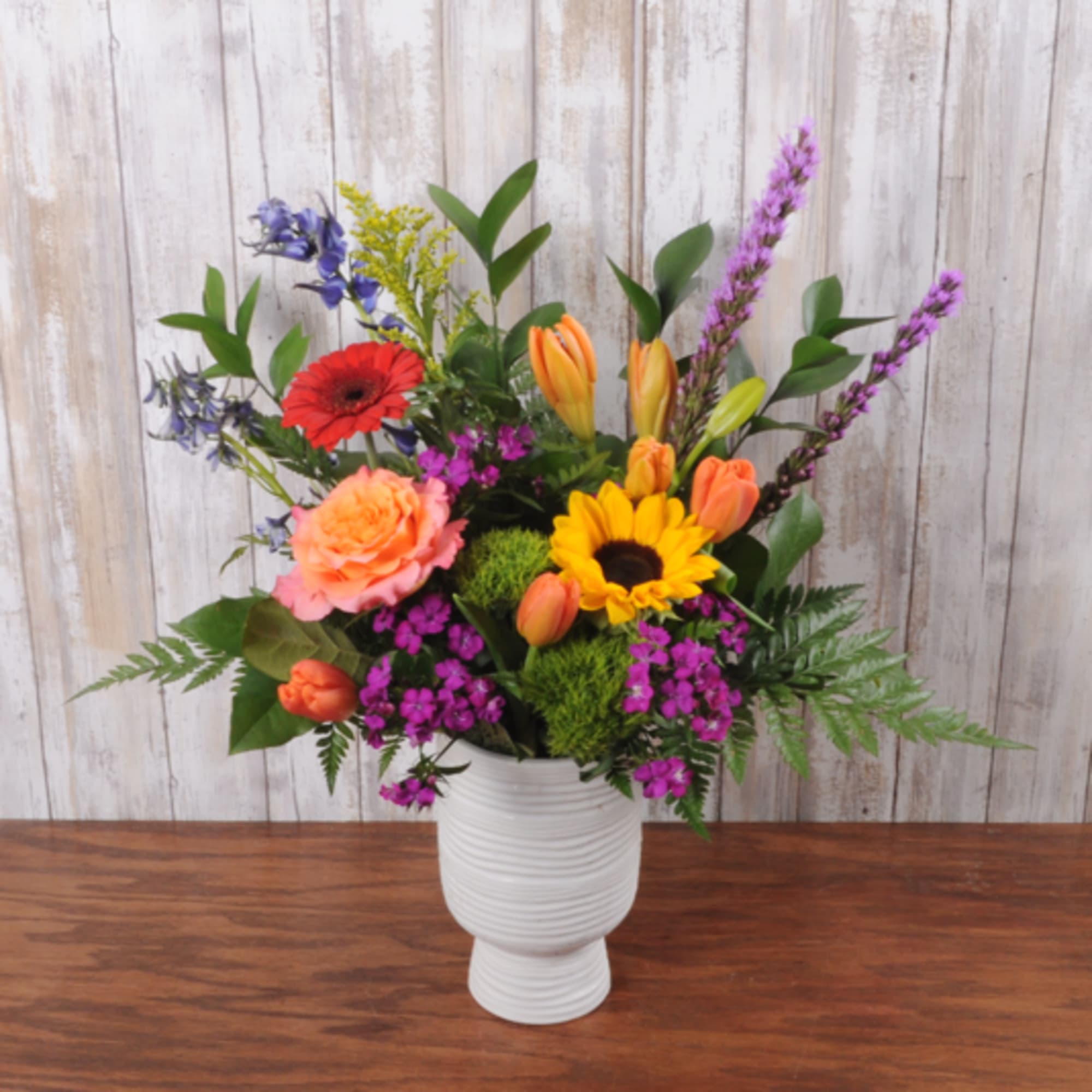 A burst of sunlit color-bright yellow sunflowers with coral roses, orange tulips