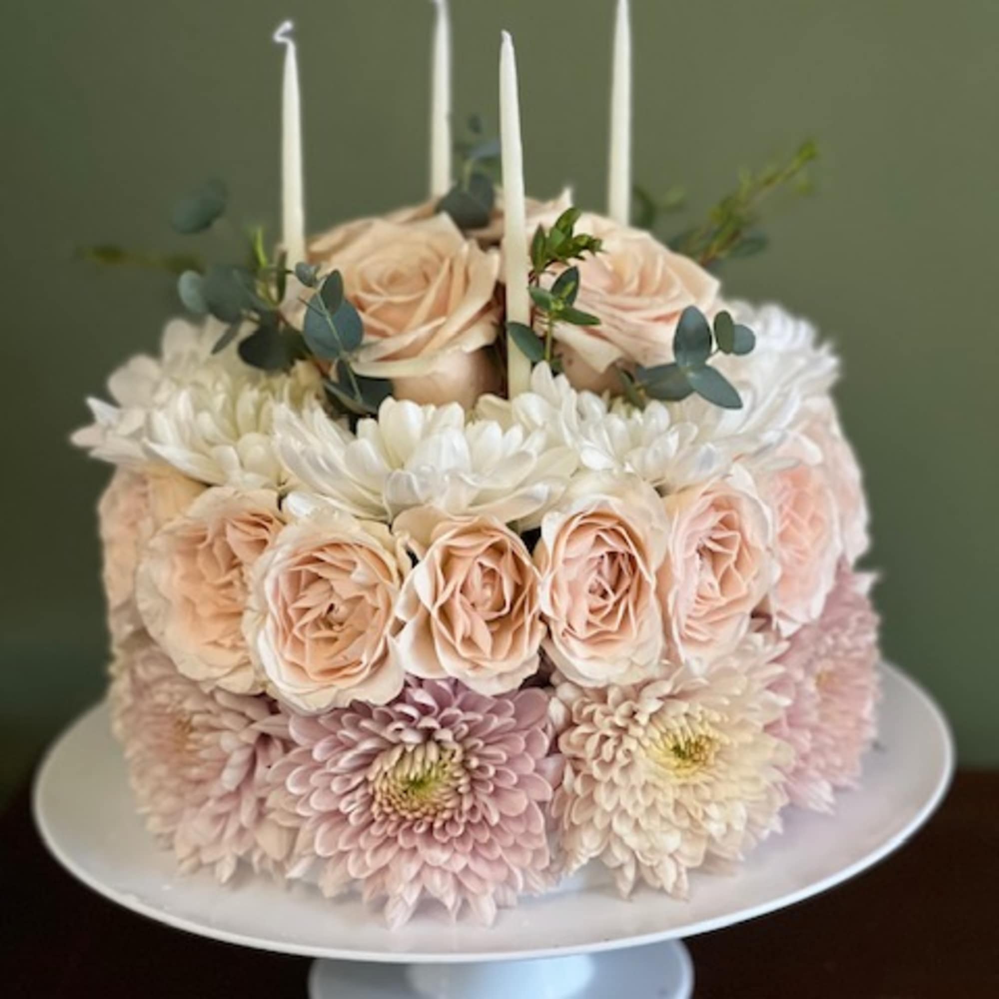 Round floral cake with pale roses, chrysanthemums, and white candles