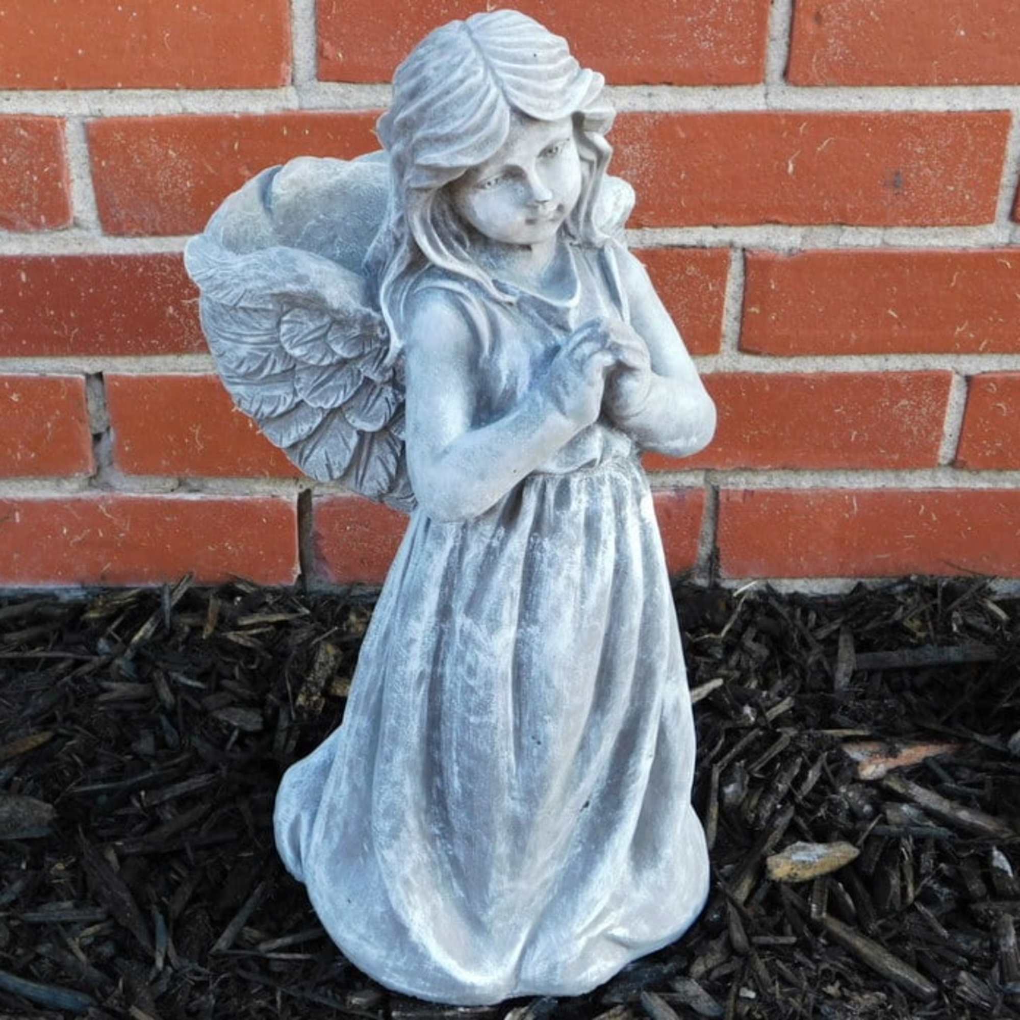 Small angel statue in a dress against a brick wall