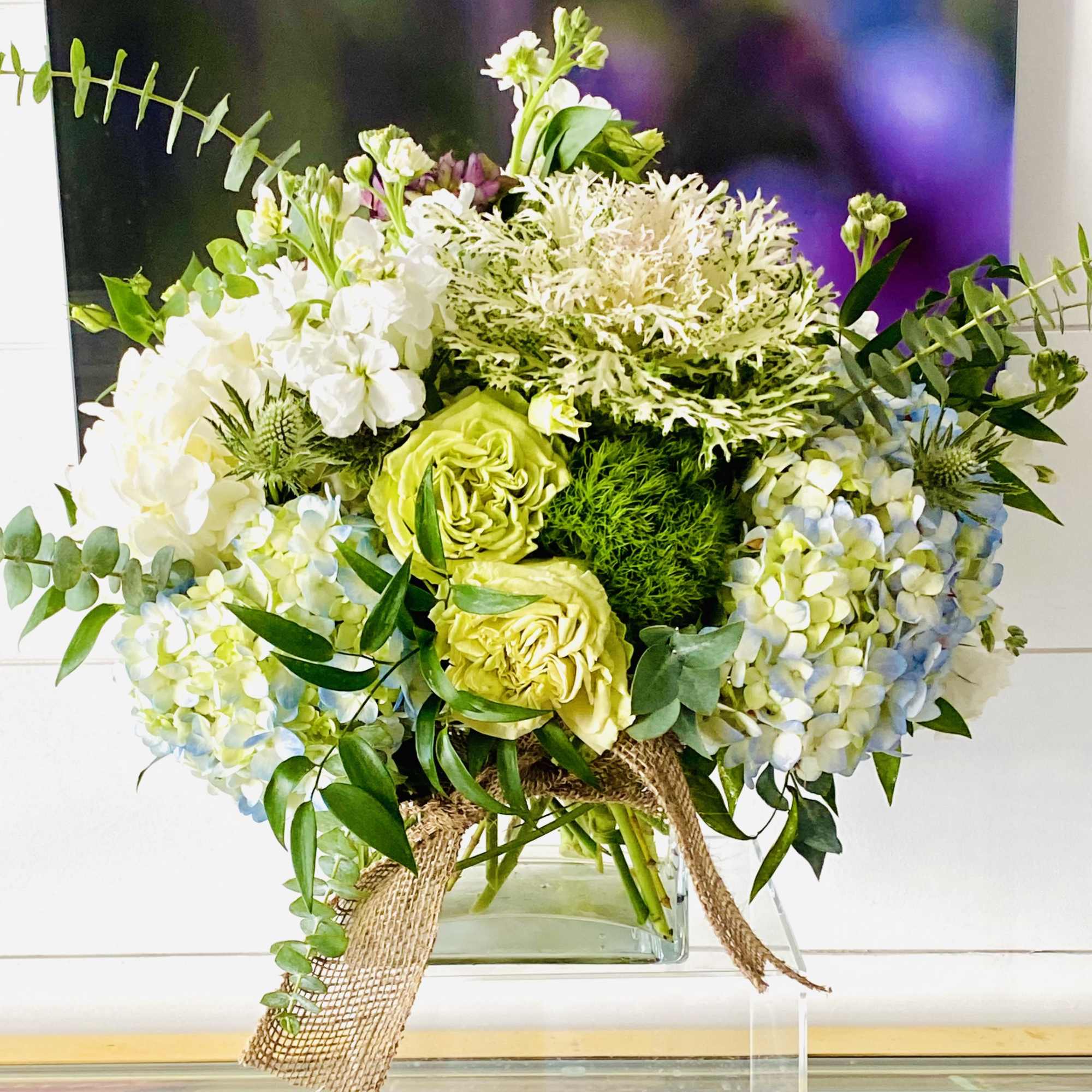 Bouquet of white and pale green flowers in a glass vase with burlap ribbon