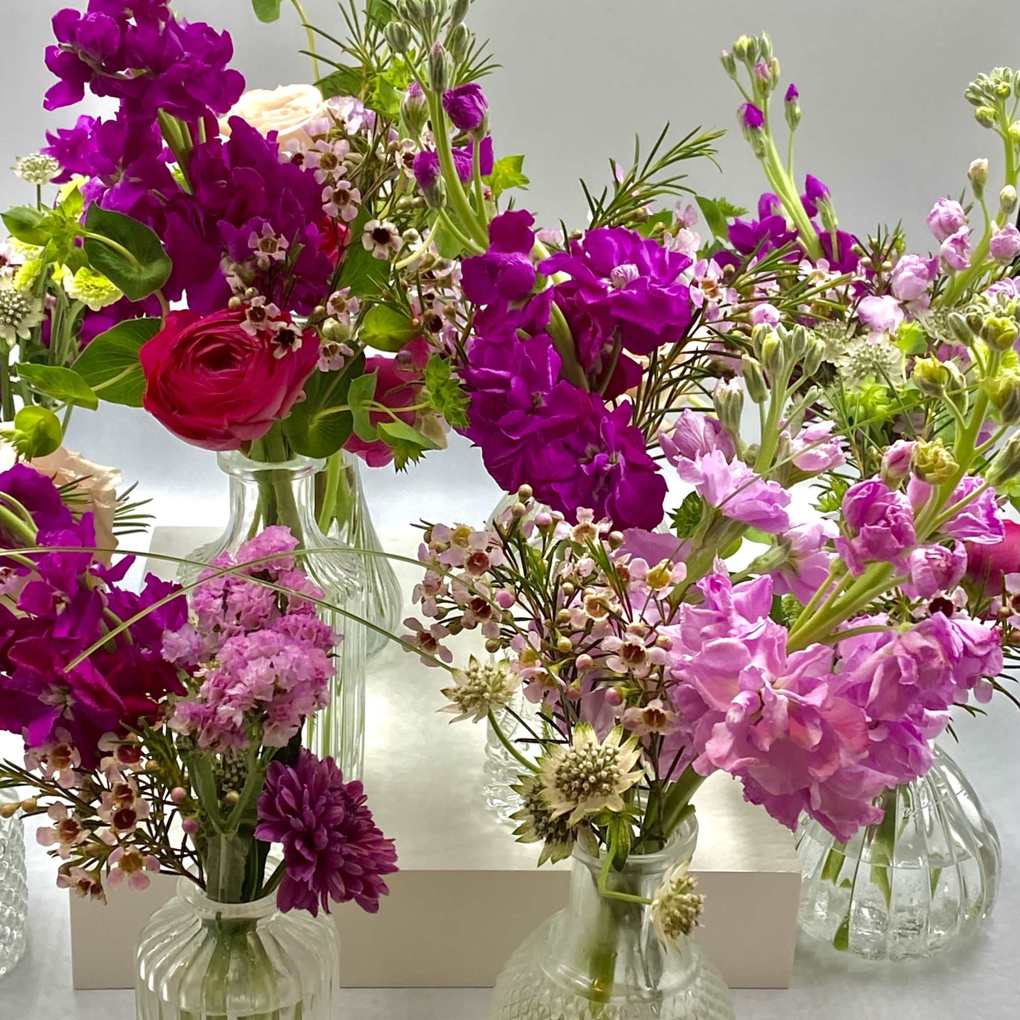 Assorted pink and purple flower arrangements in small glass vases