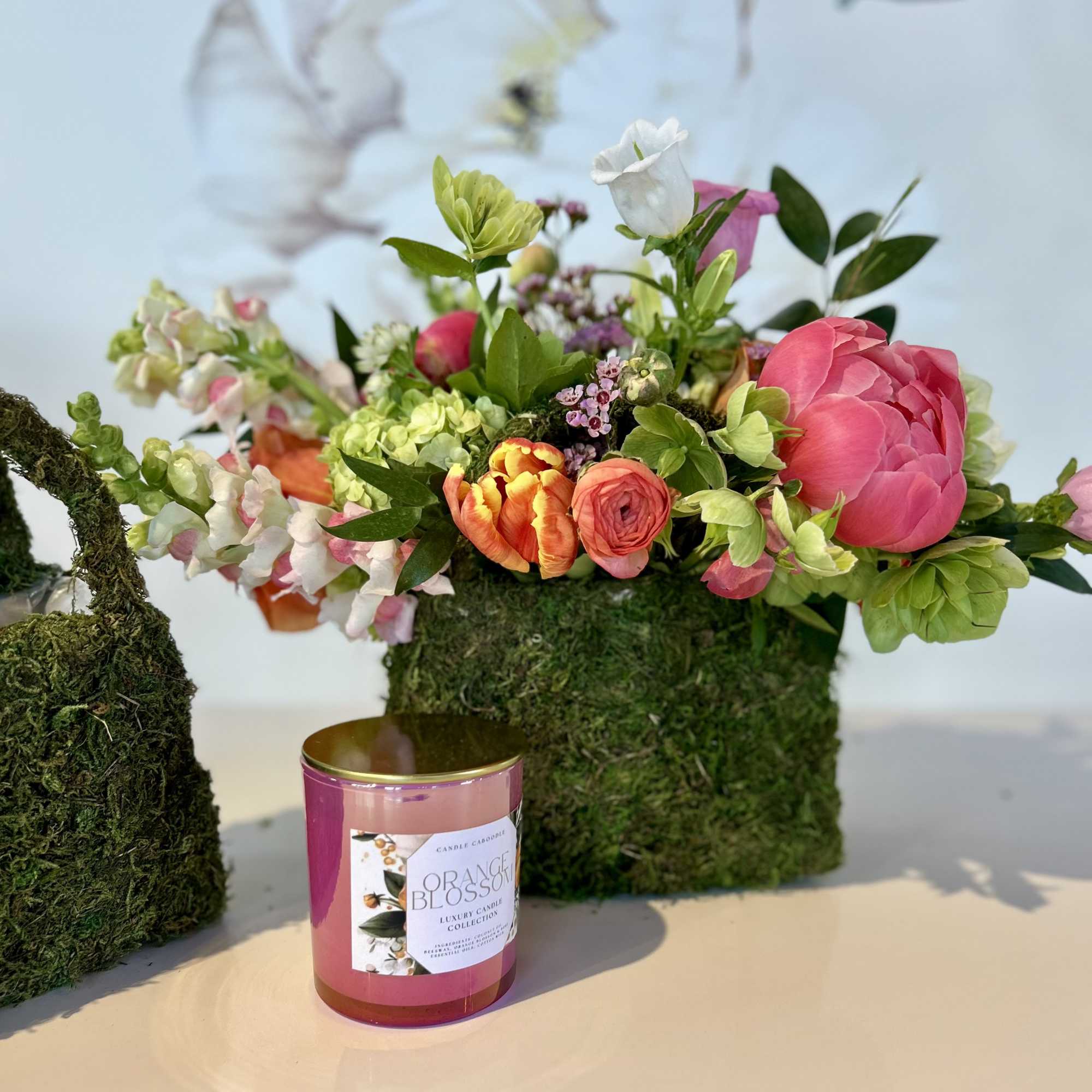 Mixed floral arrangement in a moss-covered container with a pink candle in front