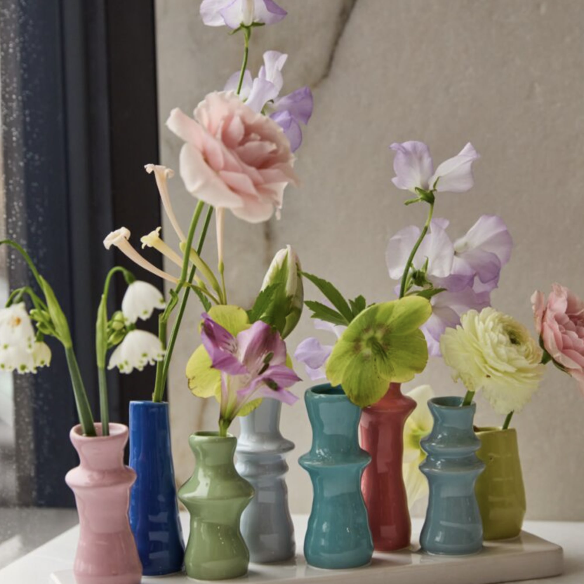 Small flowers arranged in colorful bud vases on a tray