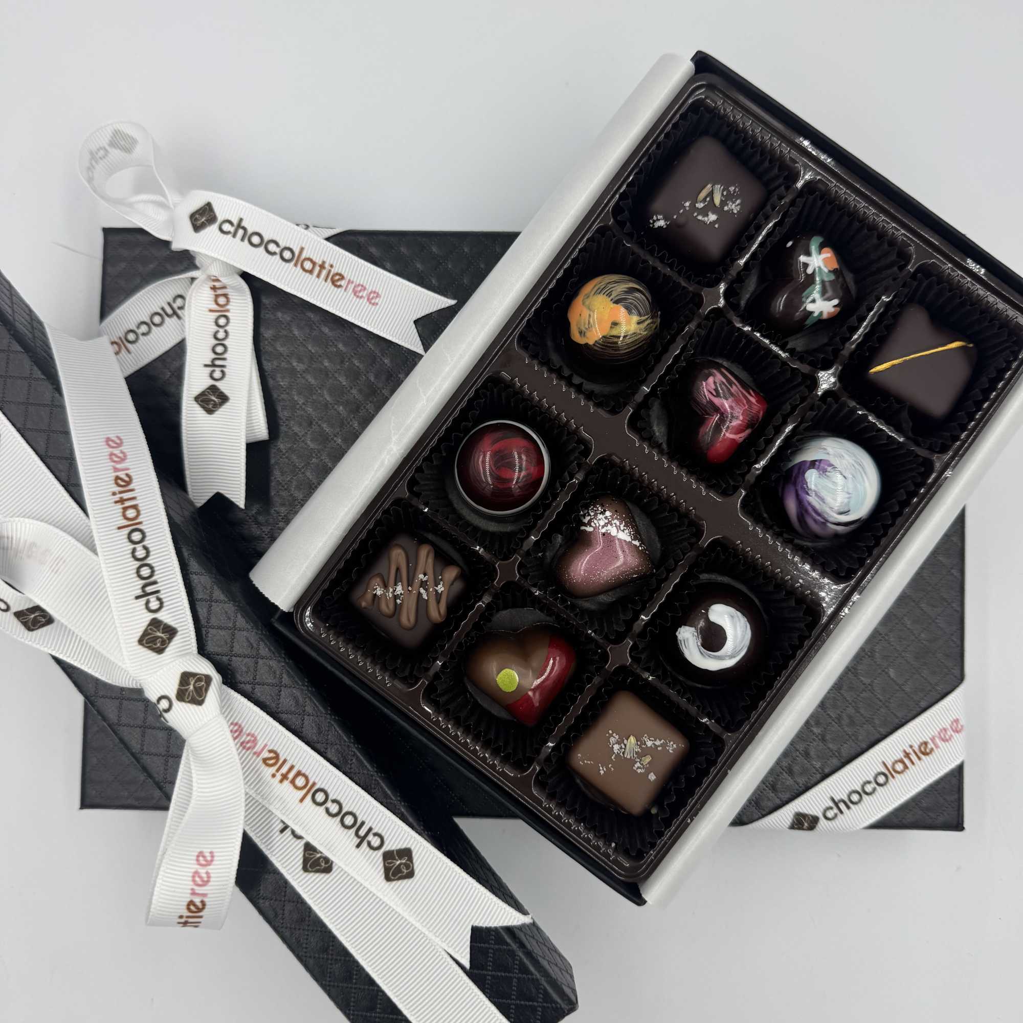 Box of assorted artisan chocolates in a black textured gift box with white logo ribbons
